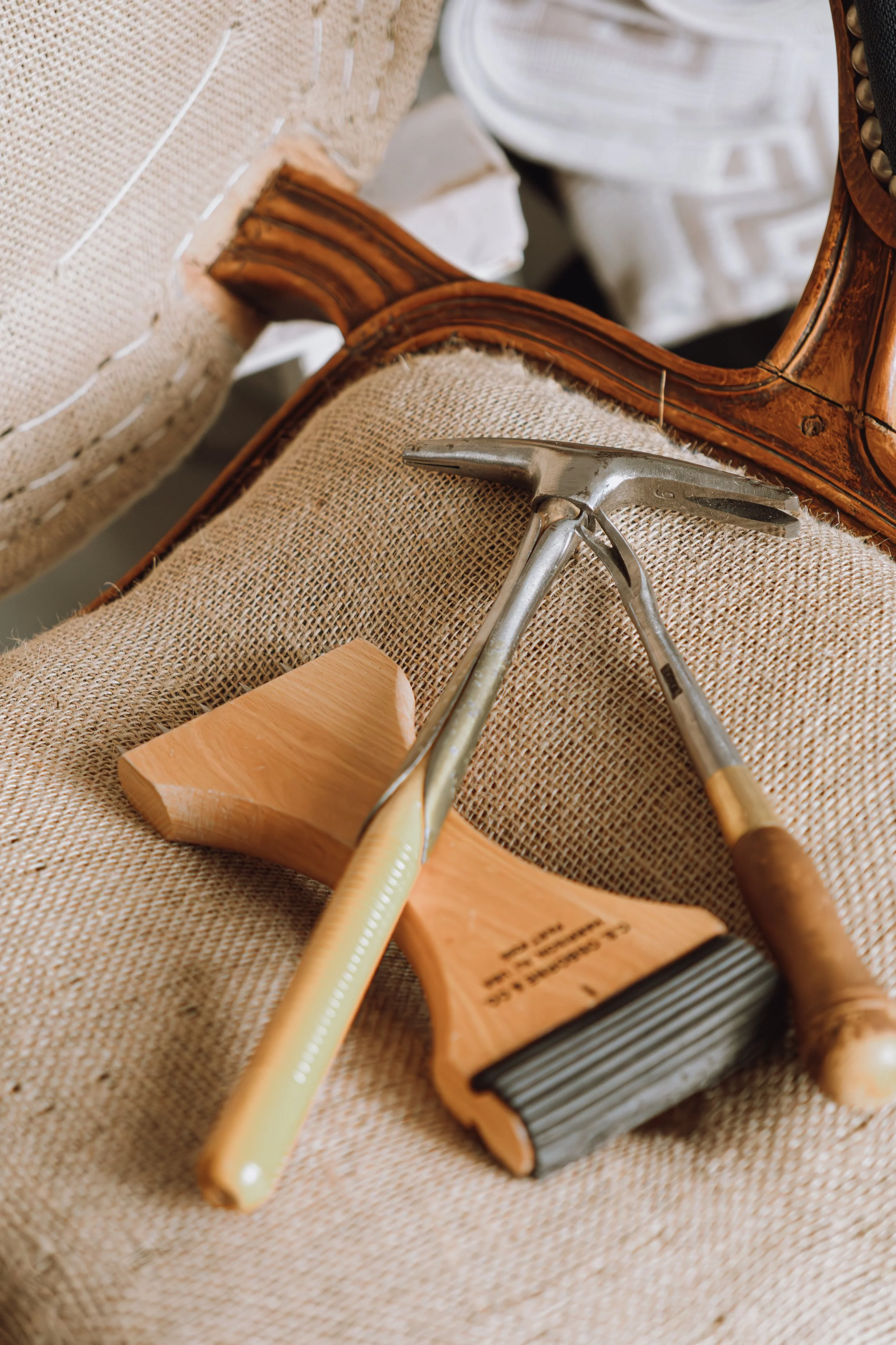 Un marteau et un outil en bois reposent sur un tissu beige, avec un fauteuil en bois et tissu en arrière-plan.