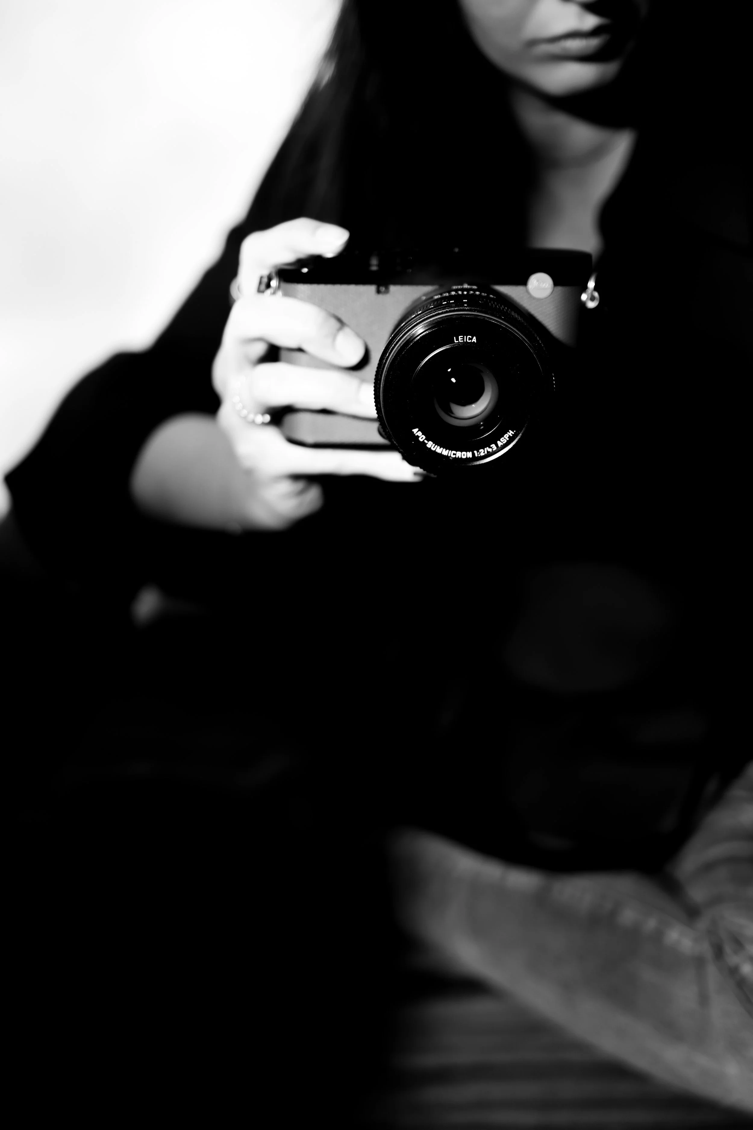 Schwarz-weiß-Foto einer Person, die eine Kamera aufnimmt, nur teilweise sichtbar mit Fokus auf die Kamera und die Hand, die sie hält.