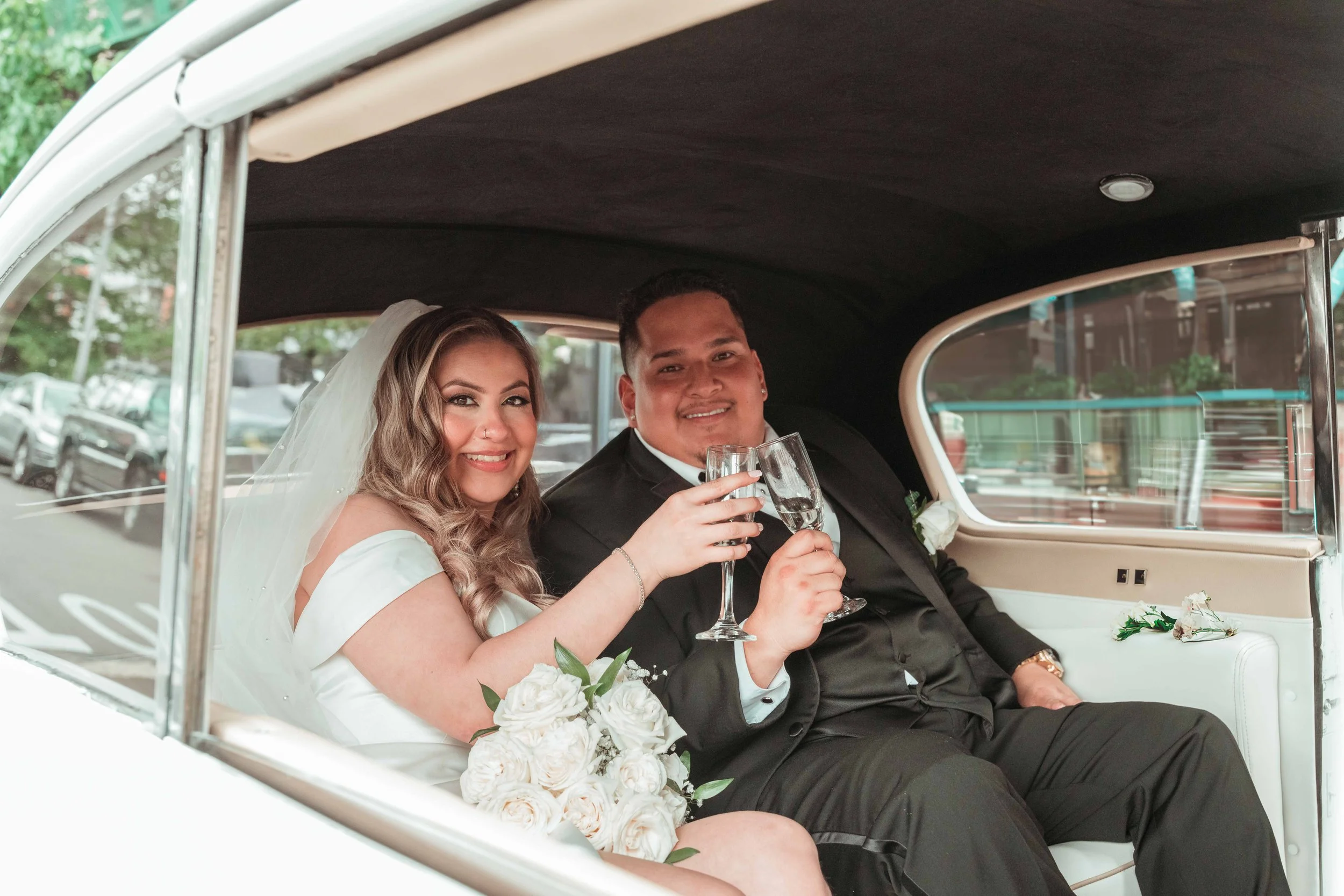 Una pareja de recién casados sonríe en una limusina blanca mientras brindan con unas copas. Ella lleva un vestido de novia y él, un traje negro.