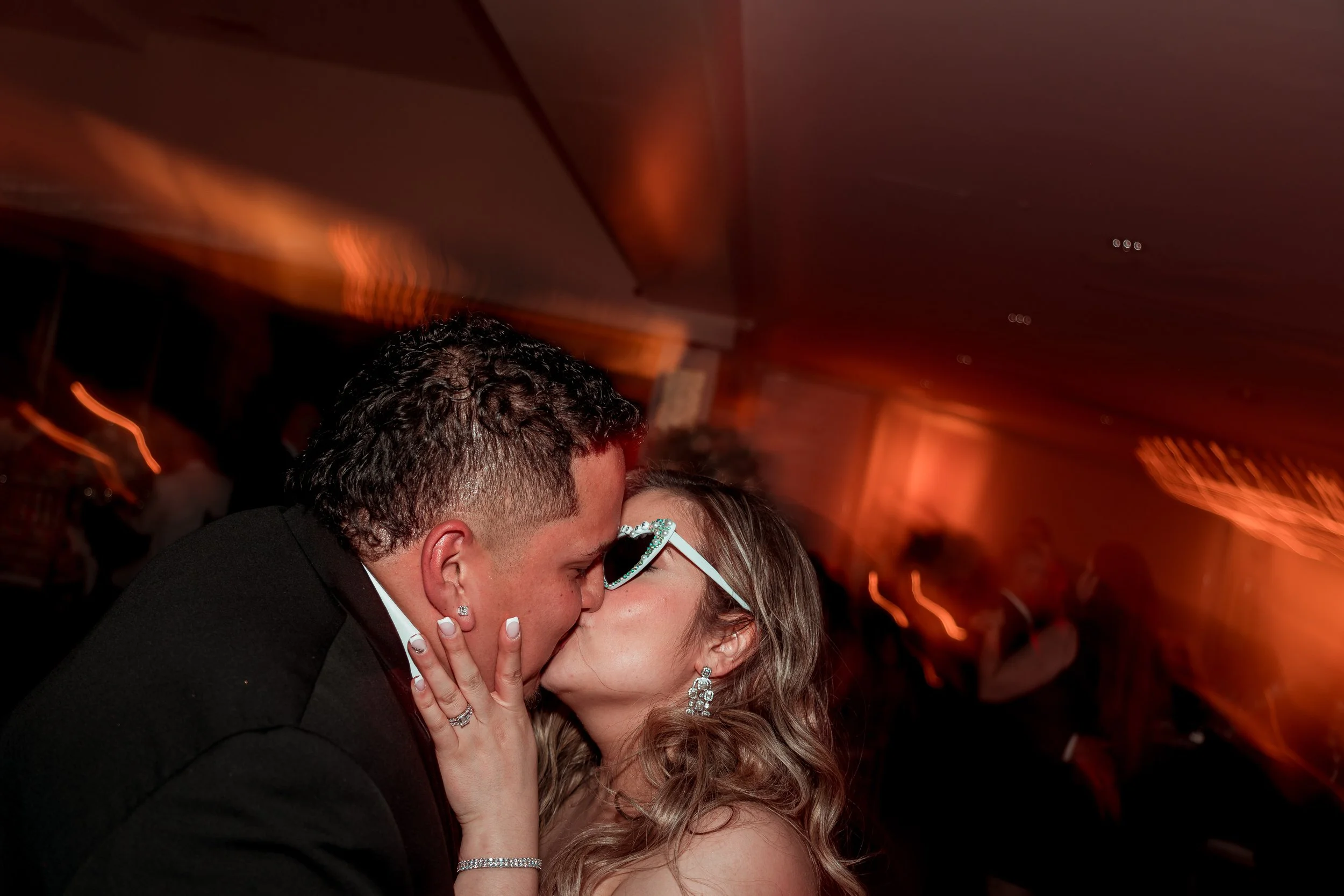 Una pareja se está besando en un ambiente con una iluminación cálida y una decoración elegante, probablemente en una fiesta o un evento formal.