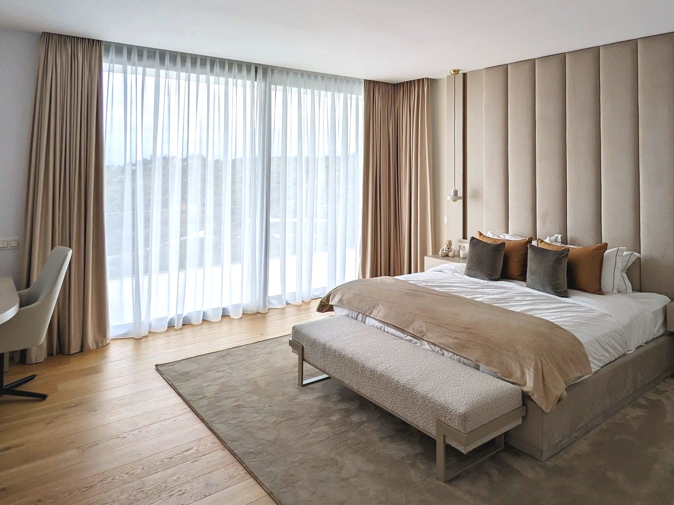 Habitación moderna con cama abatible y ventanas grandes con cortinas beige y cortinas transparentes.