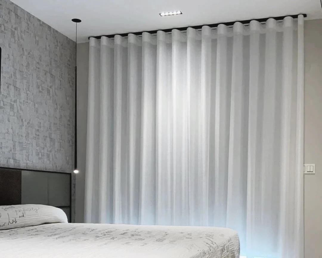 Cortinas blancas en una habitación moderna con pared de piedra y cama con sábanas blancas.