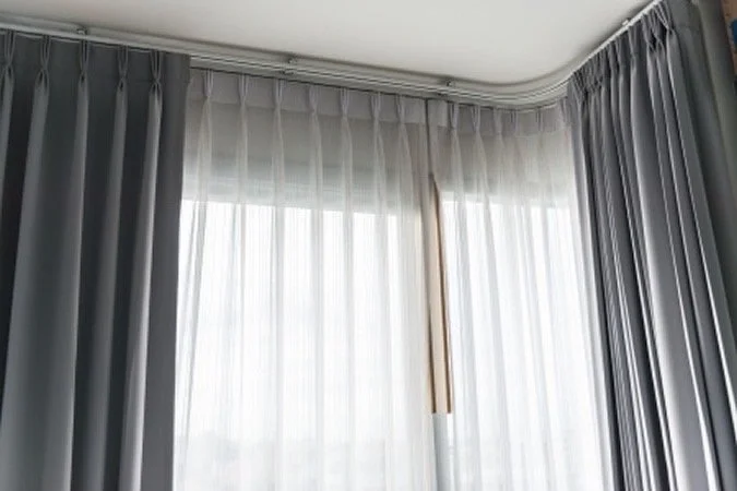Ventana cubierta con cortinas blancas y cortinas grises en una habitación