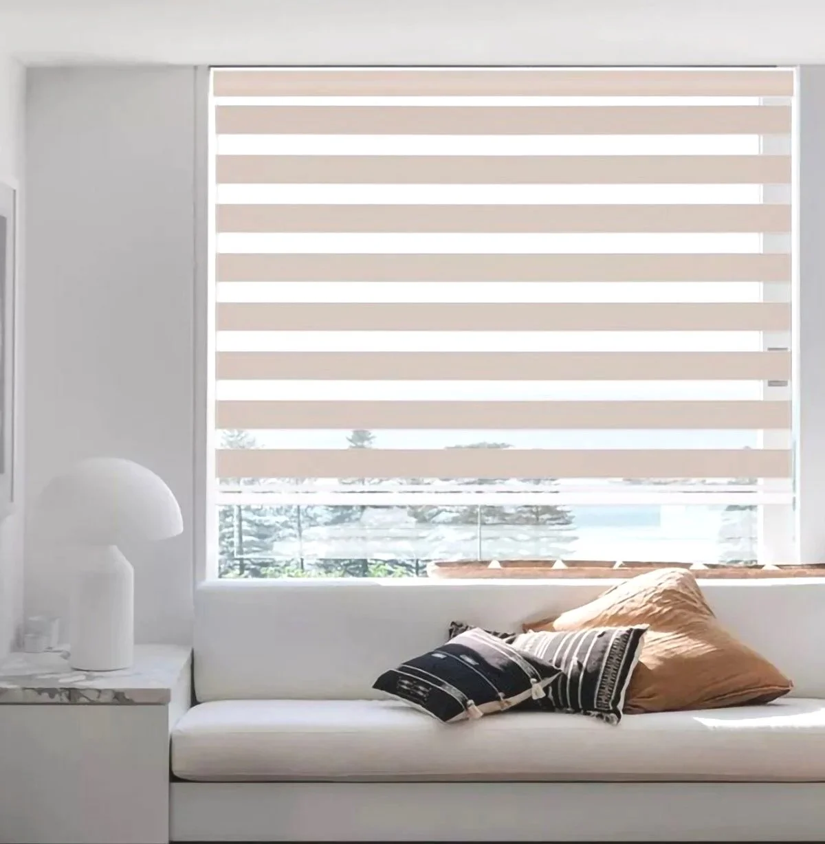 Sala moderna con sofá blanco, almohadas negras y beige, cortinas horizontales beige, vista al exterior con árboles y mar