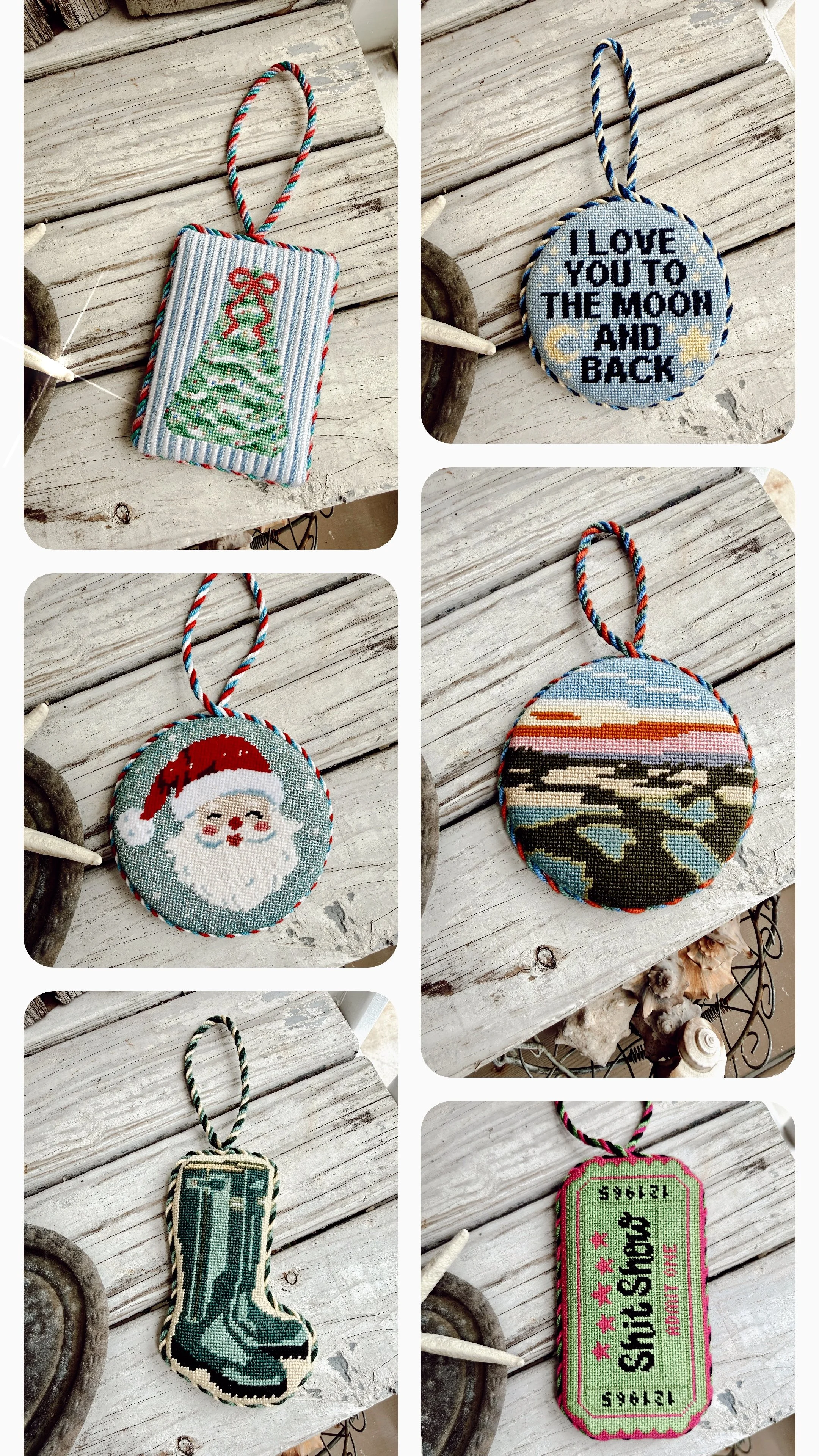 Collection of six needlepoint ornaments with custom cording on a rustic wooden surface. Designs include a Christmas tree, a winter scene with the message "I love you to the moon and back," Santa Claus, a sunset over water,
