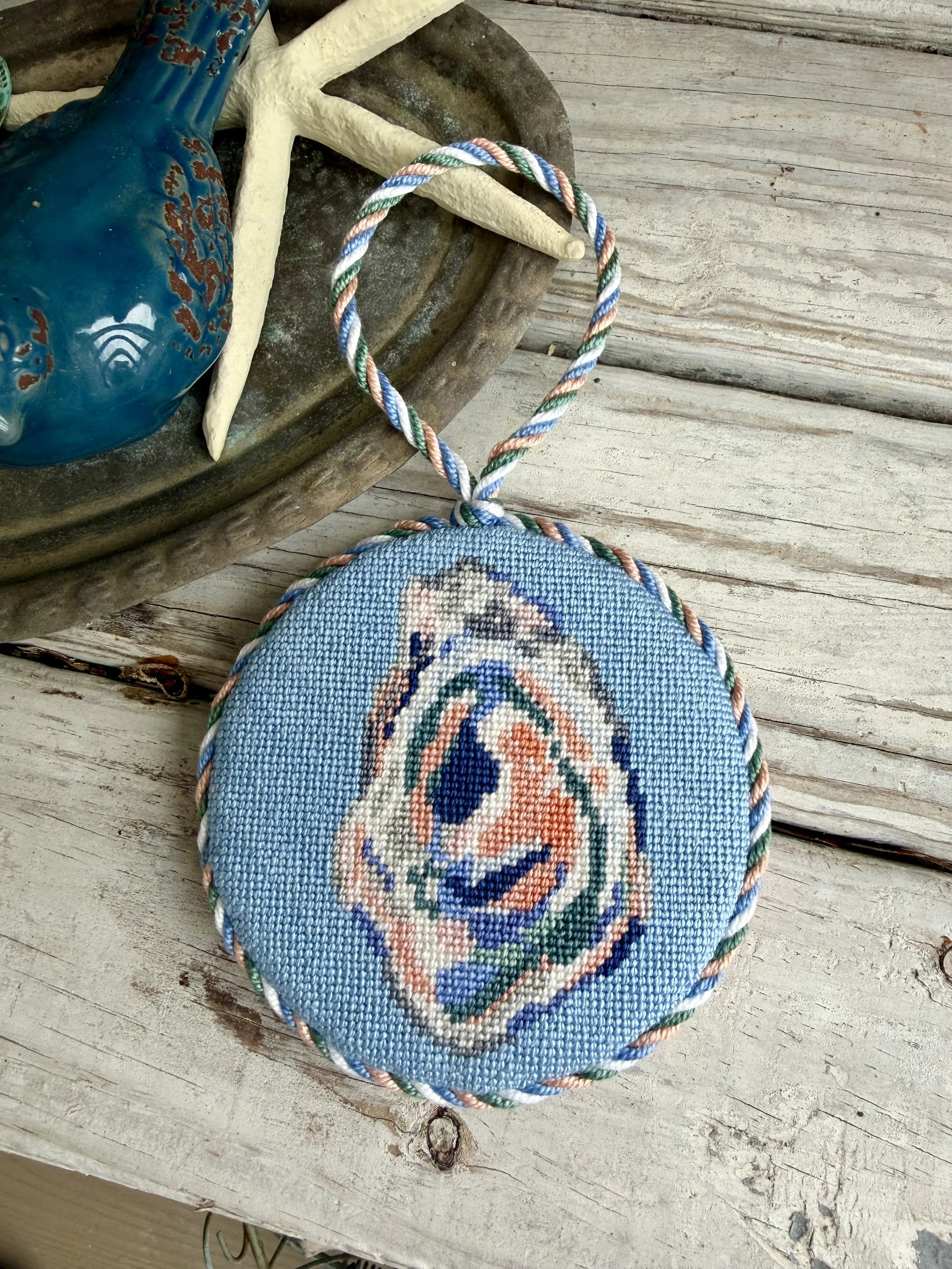 Round Finished Needlepoint Ornament with custom cording. Pastel Oyster image hand stitched Finished with The Salty Stitchery
