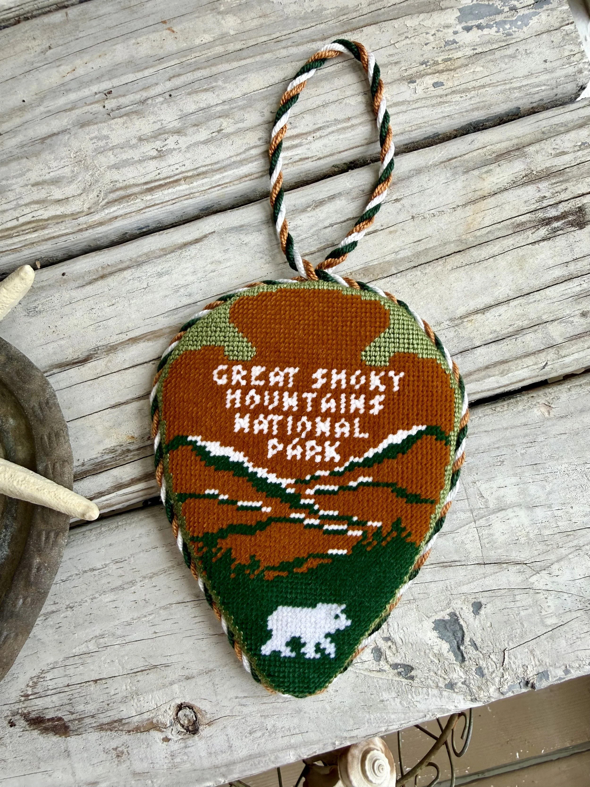  National Park finished needlepoint ornament, with a custom cording loop  The ornament has an orange, green, and white needlepoint  design with the words 'Great Smokey National Park' Finished with The Salty Stitchery