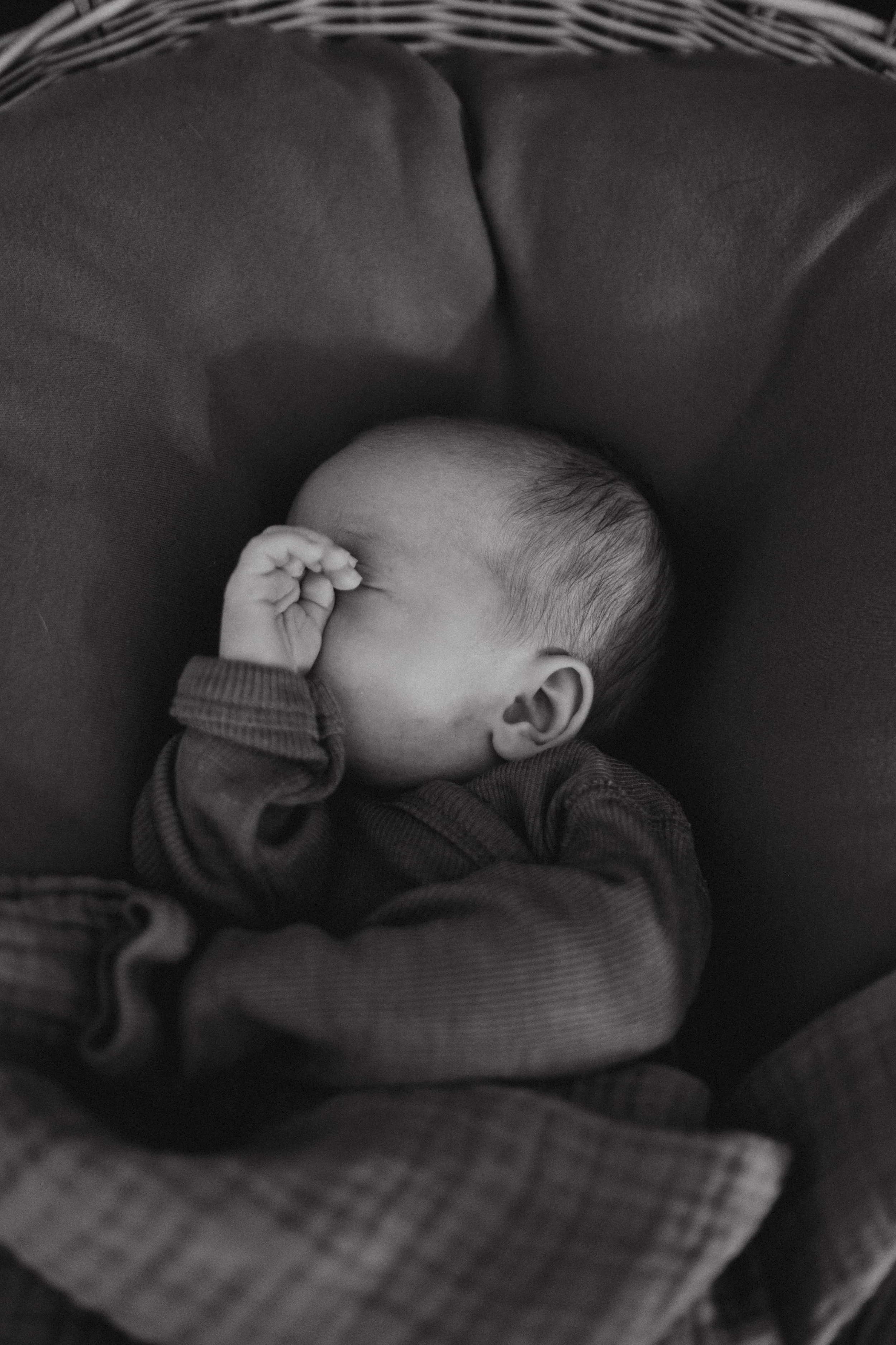 Ein Baby schläft eingekuschelt in dunkler Kleidung, in einer dunklen Umgebung, schwarz-weiß aufgenommen.
