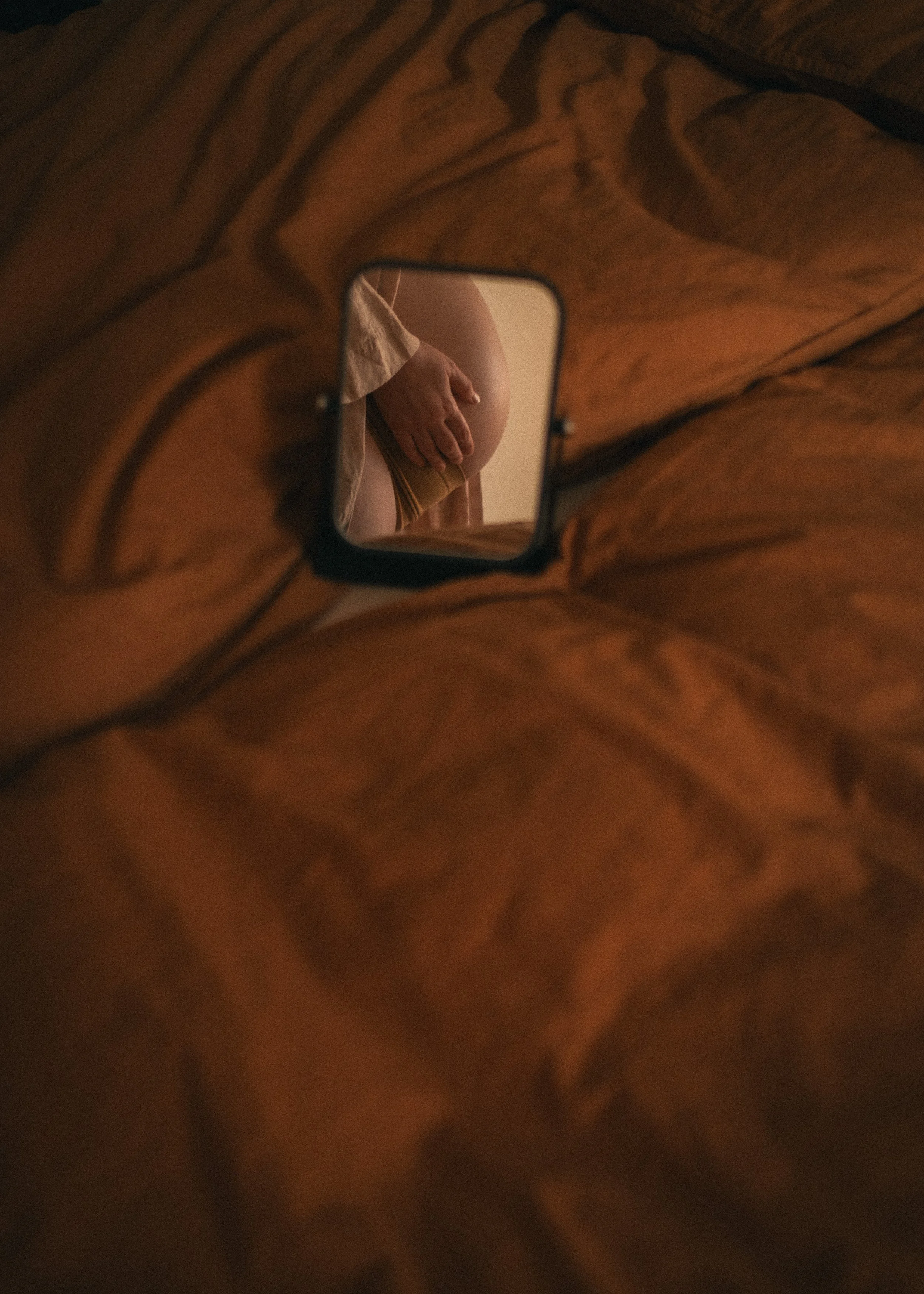 Ein Spiegel auf einem Bett, der einen Teil eines nackten Körpers und eine Hand zeigt.