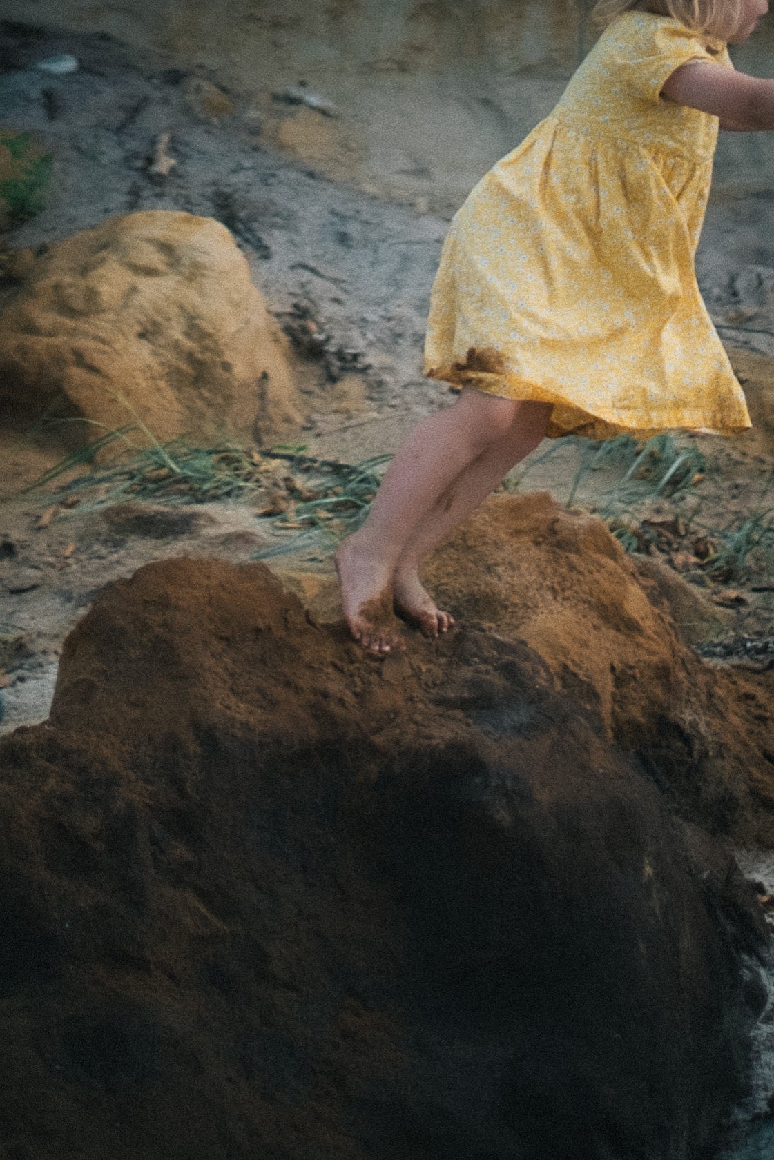 Ein Kind in einem gelben Kleid läuft über Felsen und Sand im Freien.