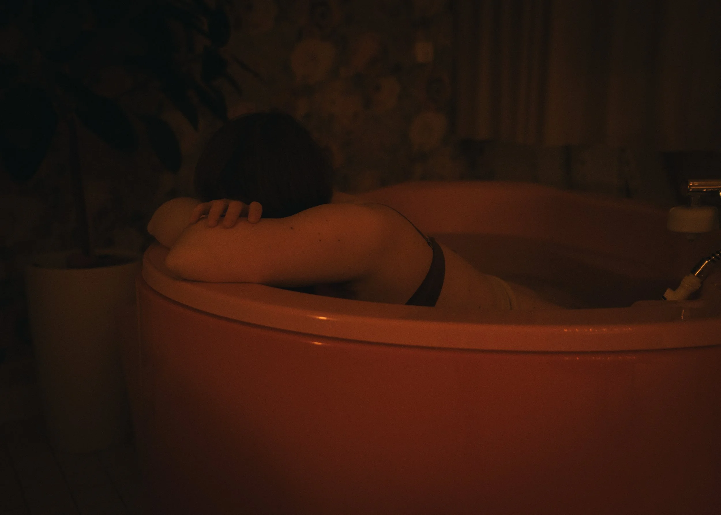 Person liegt in einer rosa Badewanne, die sich in einem dunklen Raum befindet.