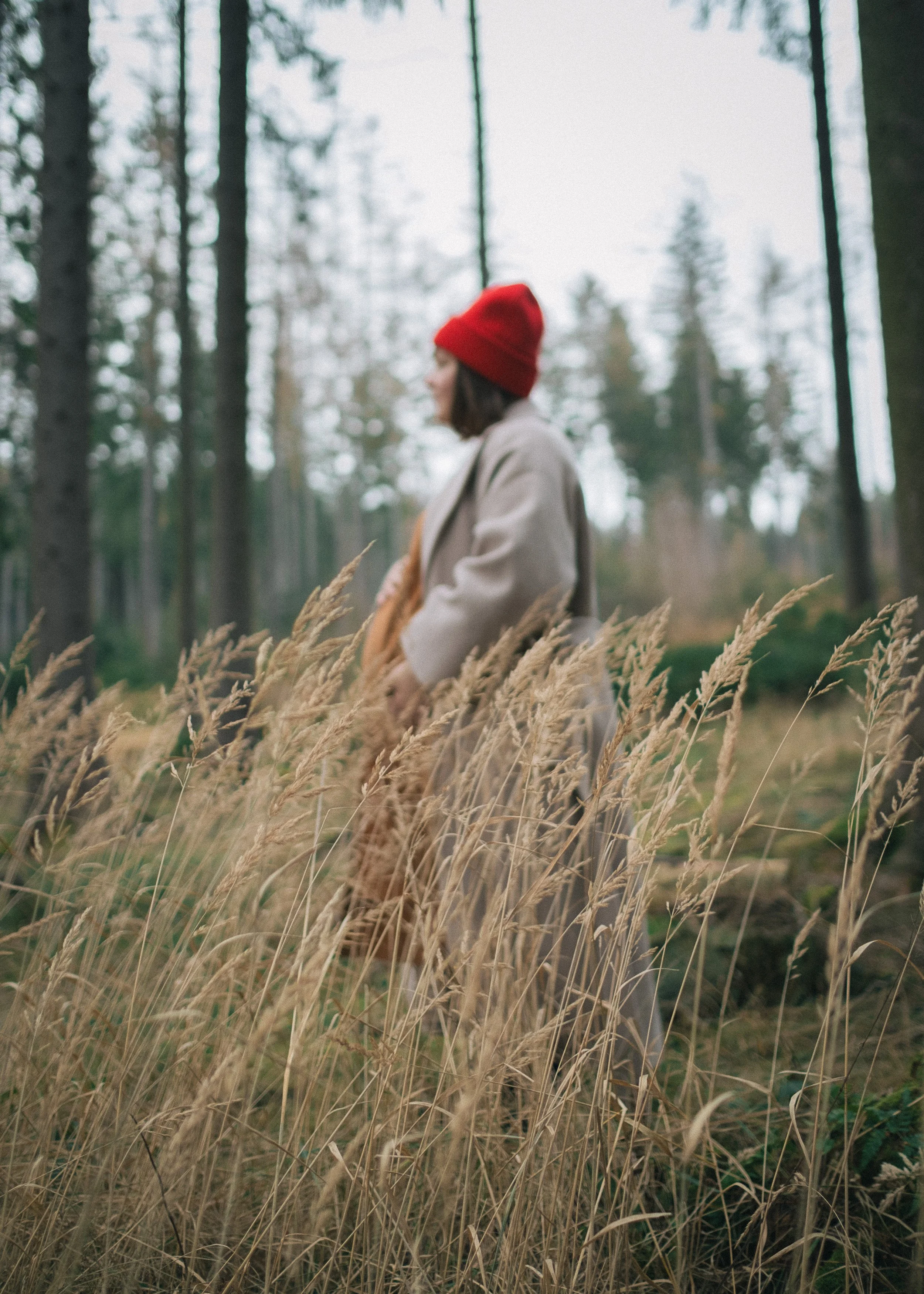 Frau mit roten Mütze im Wald, umgeben von Gräsern.