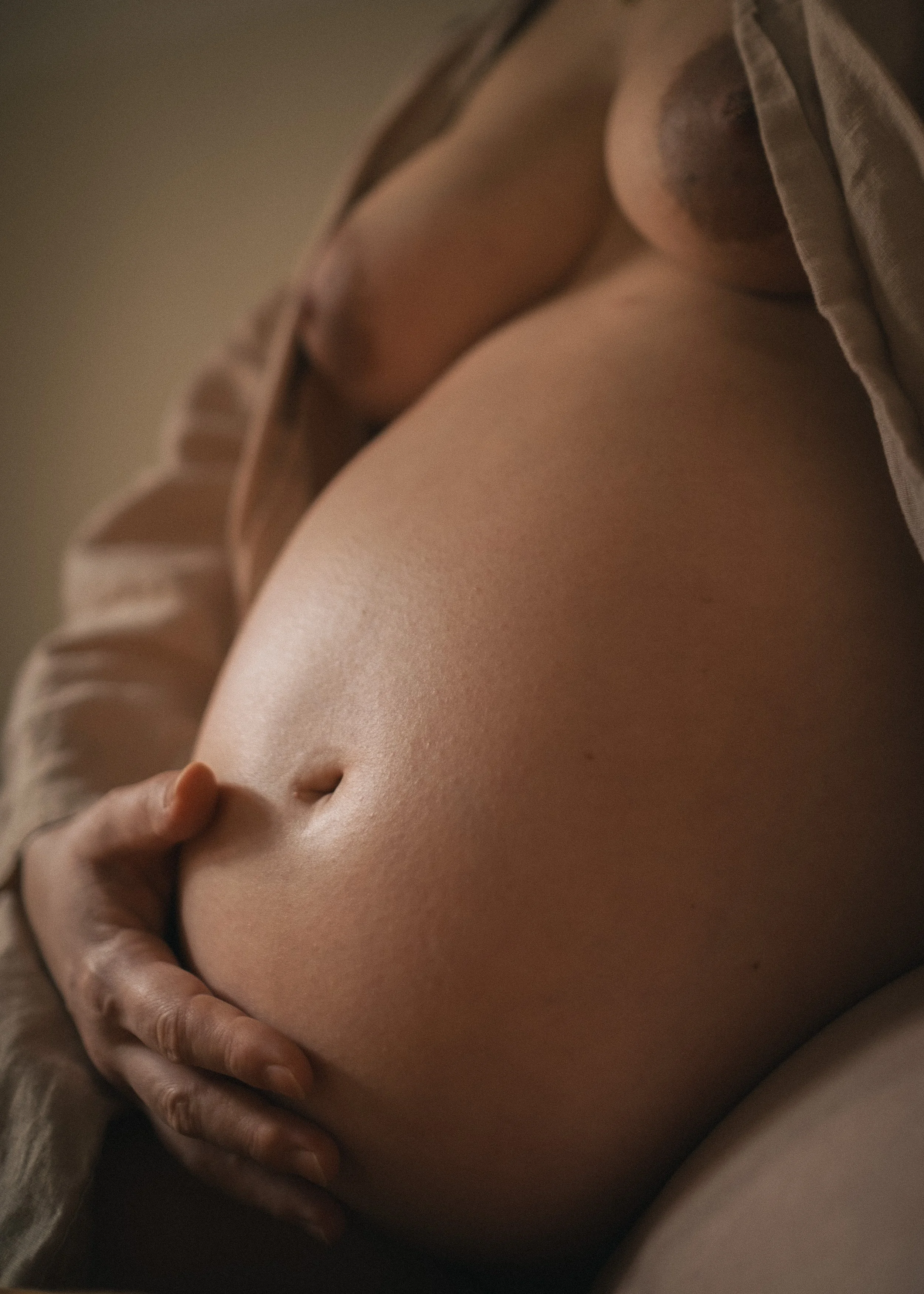 Nahaufnahme eines schwangeren Bauchs mit Hand, der den Bauch hält, bei weicher Beleuchtung.