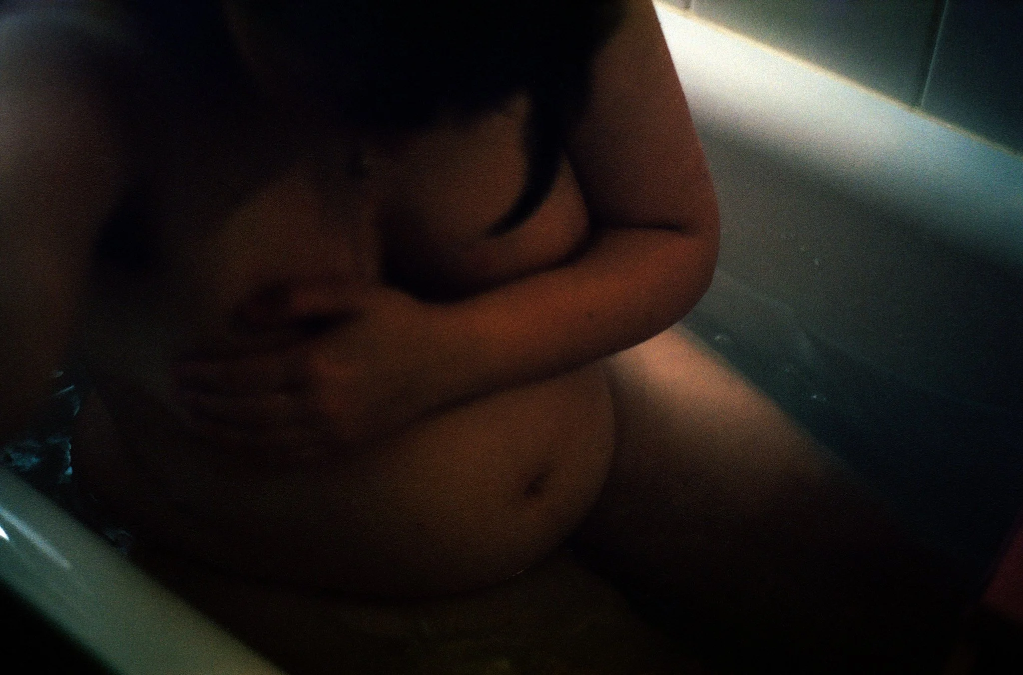 Ein Kind sitzt in einer Badewanne, das Wasser ist sichtbar und das Kind ist nackt.