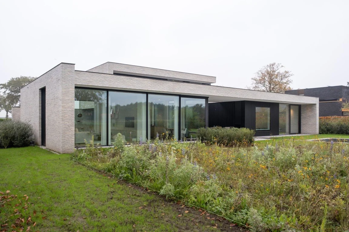 Modern house with large glass windows and a garden in the foreground.