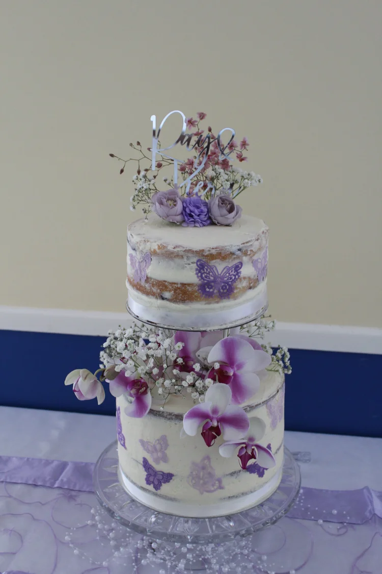 Two-tier lactose-free celebration cake decorated with lilac butterflies and fresh flowers