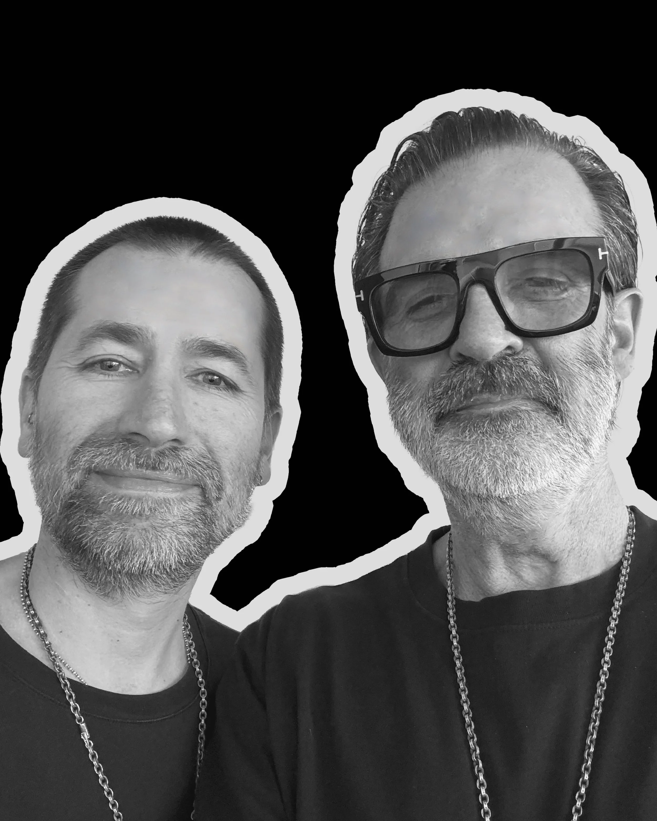 Black and white photo of two men with beards and short hair, wearing sunglasses, black t-shirts, and silver chains, against a black background.