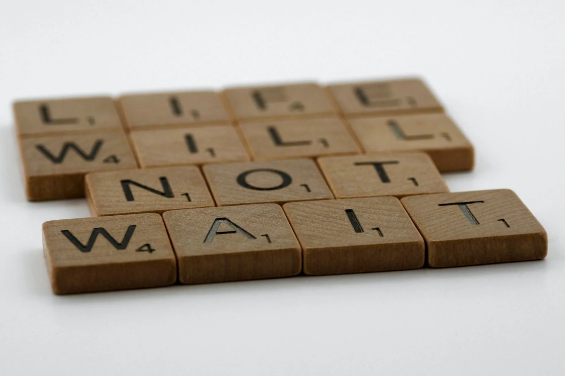 Scrabble letter tiles reading "Life will not wait"