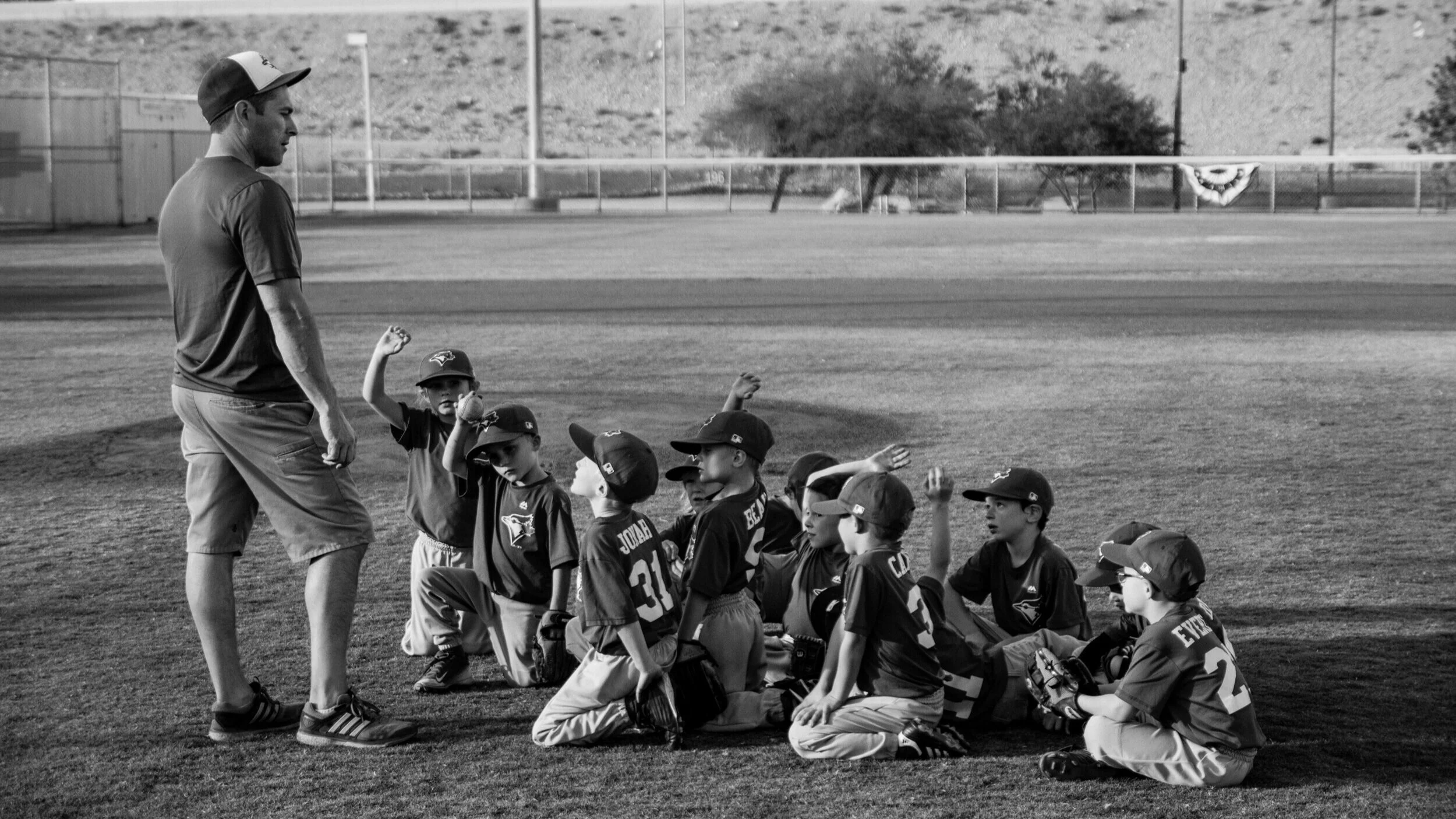 Coach stands in front of a group of boys in baseball uniforms