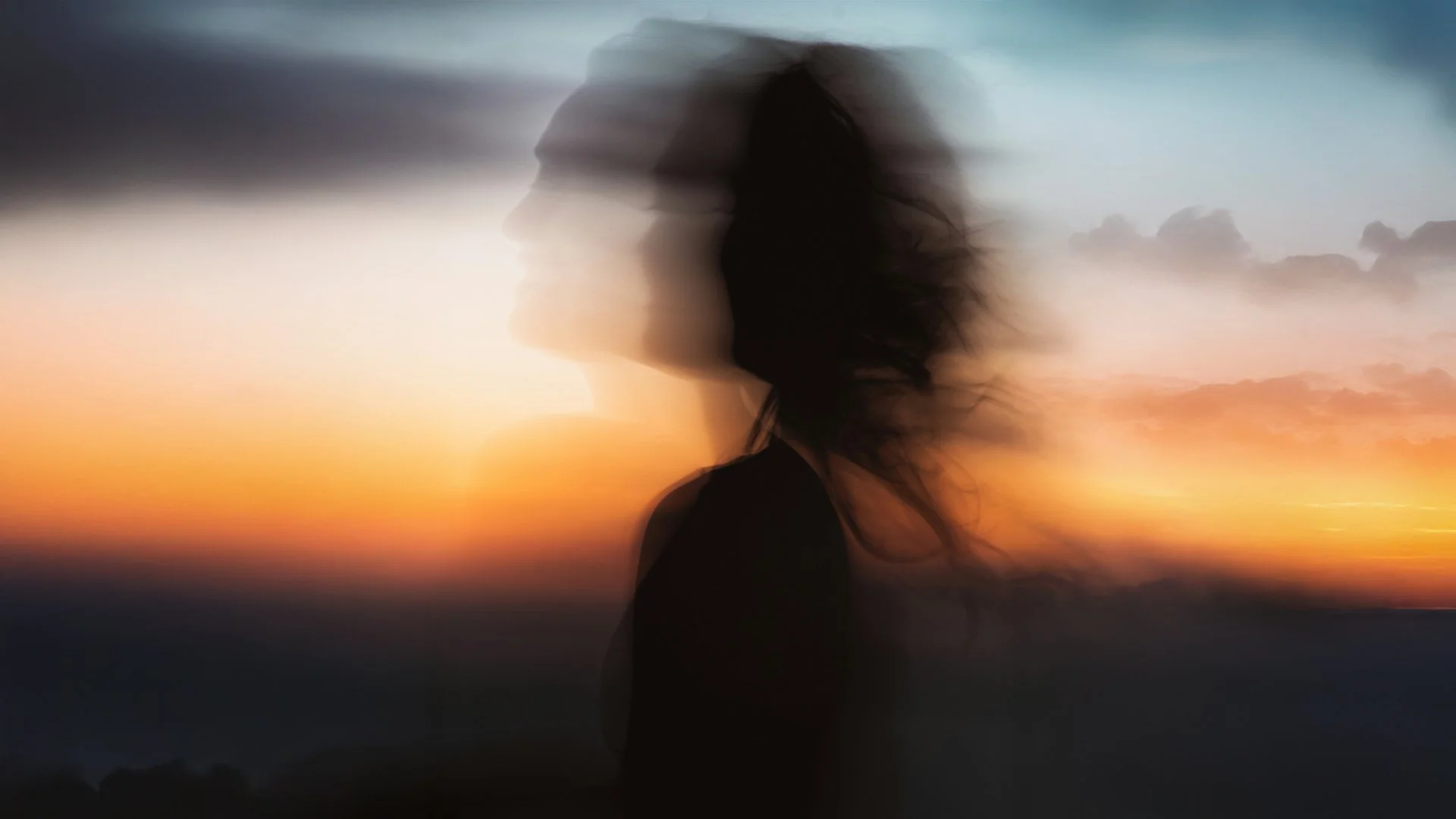 Silhouette of a woman with flowing hair against a colorful sunset sky.