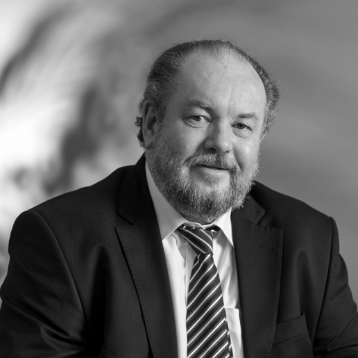 Black and white portrait of a middle-aged man with a beard, wearing a suit and tie, smiling slightly.