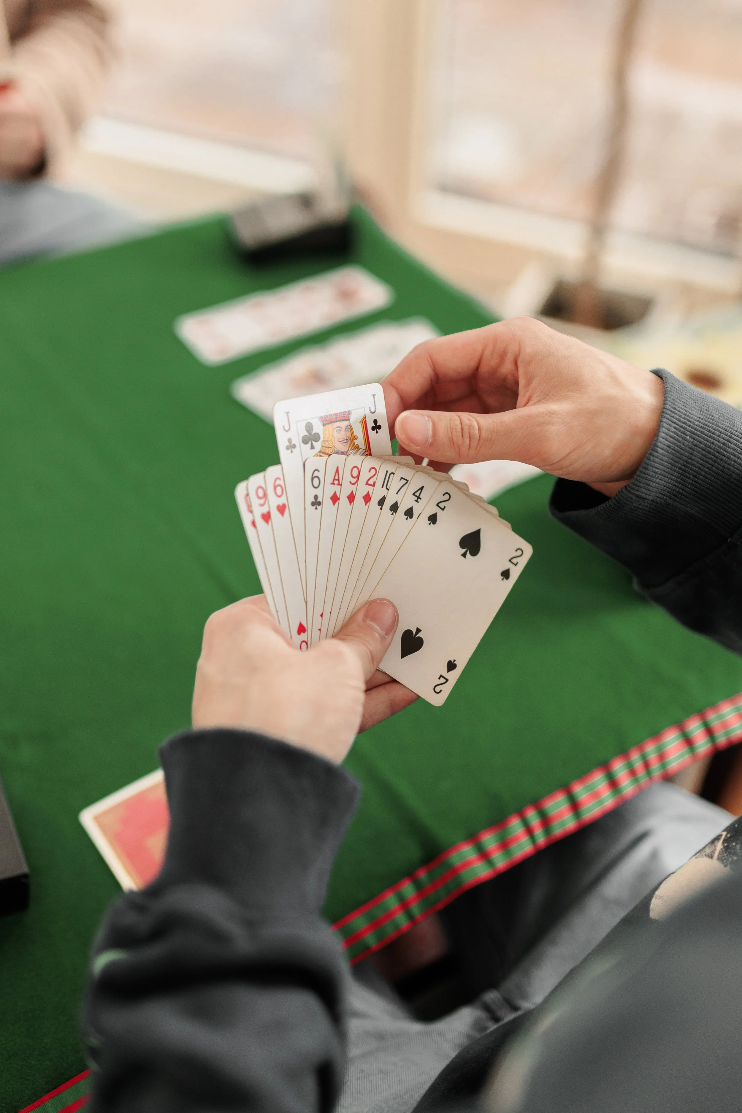 A person holding a fan of playing cards, with a green gaming table and other cards in the background.