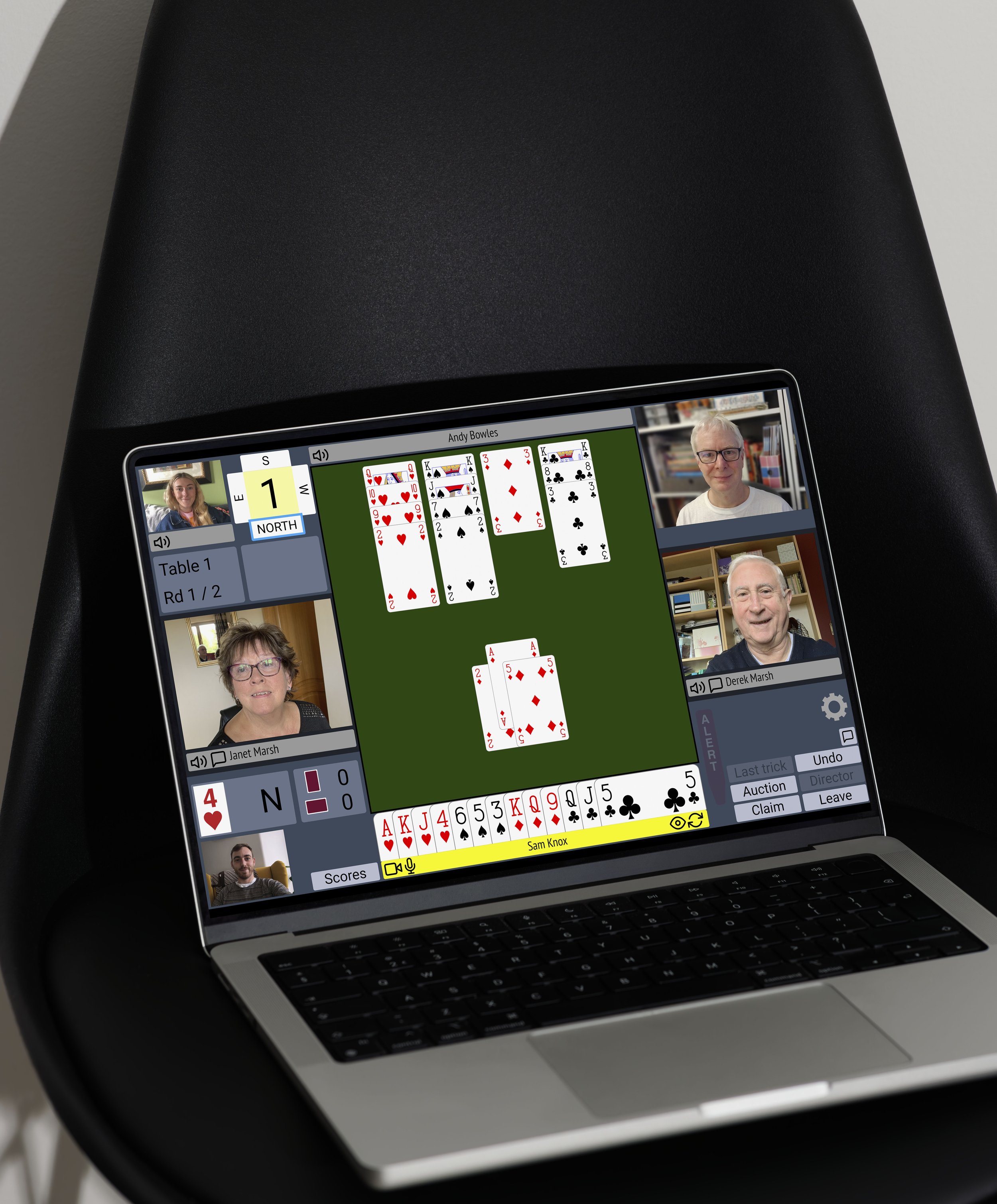 A laptop displaying an online card game with multiple players and a central tableau of played cards, in a virtual meeting setting.