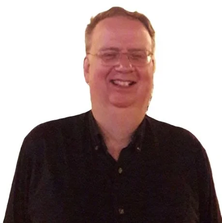 A smiling man with glasses and light skin, wearing a black button-up shirt, against a plain white background.
