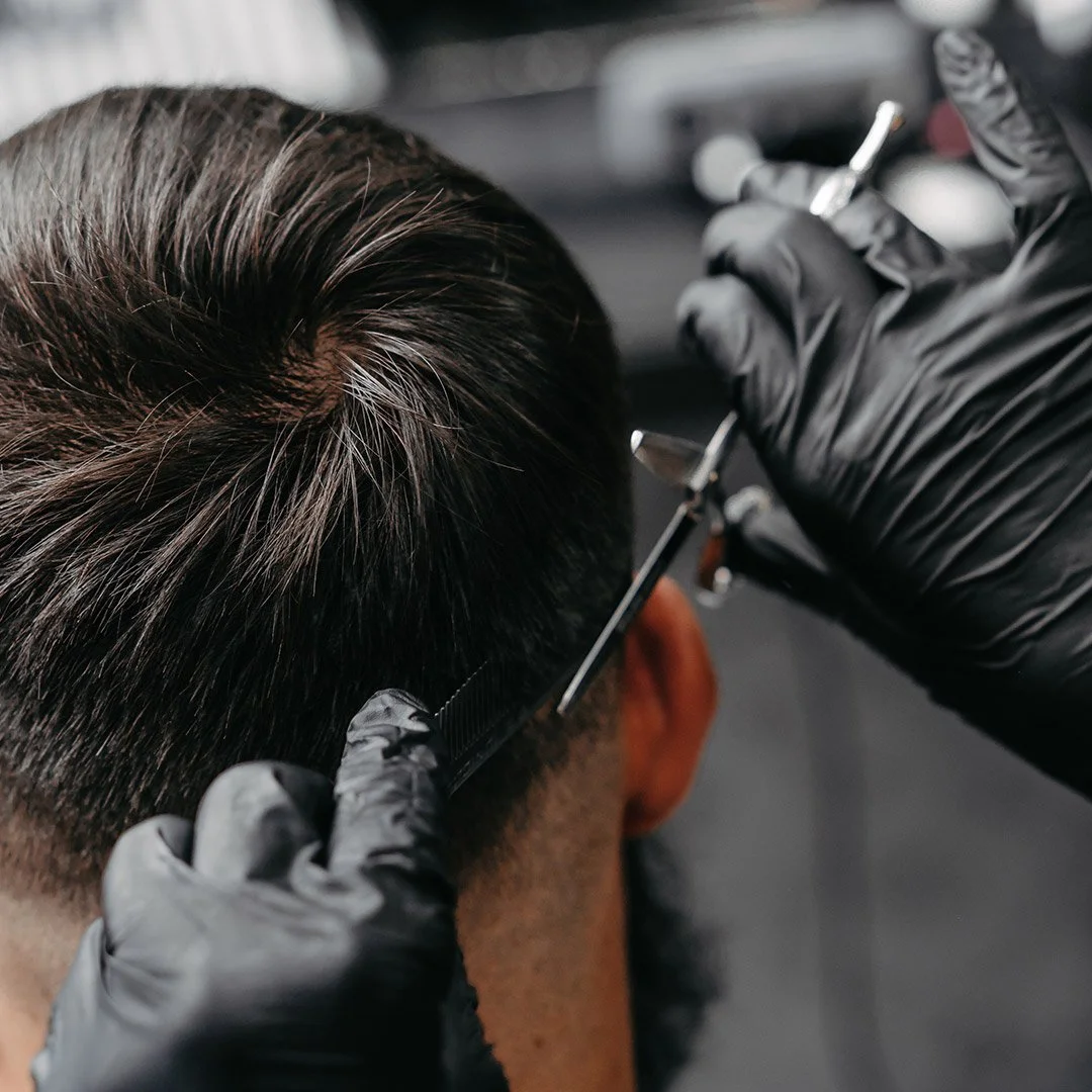 A person with dark hair getting their hair tattooed or microbladed by a technician wearing black gloves.