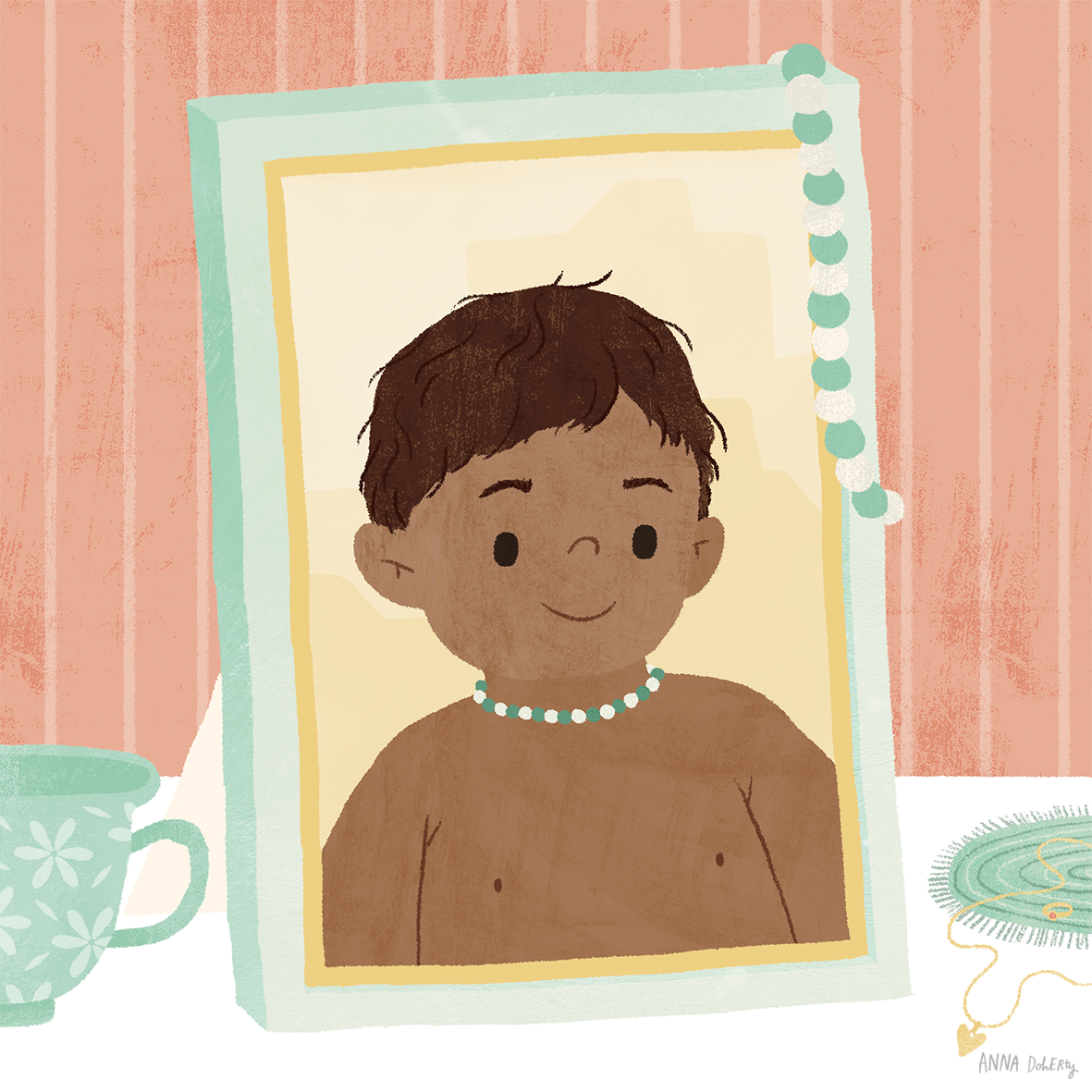 A smiling young boy with short brown hair wearing a pearl necklace, reflected in a framed mirror with a string of decorative beads, with a green mug and a plate with yarn in the background.