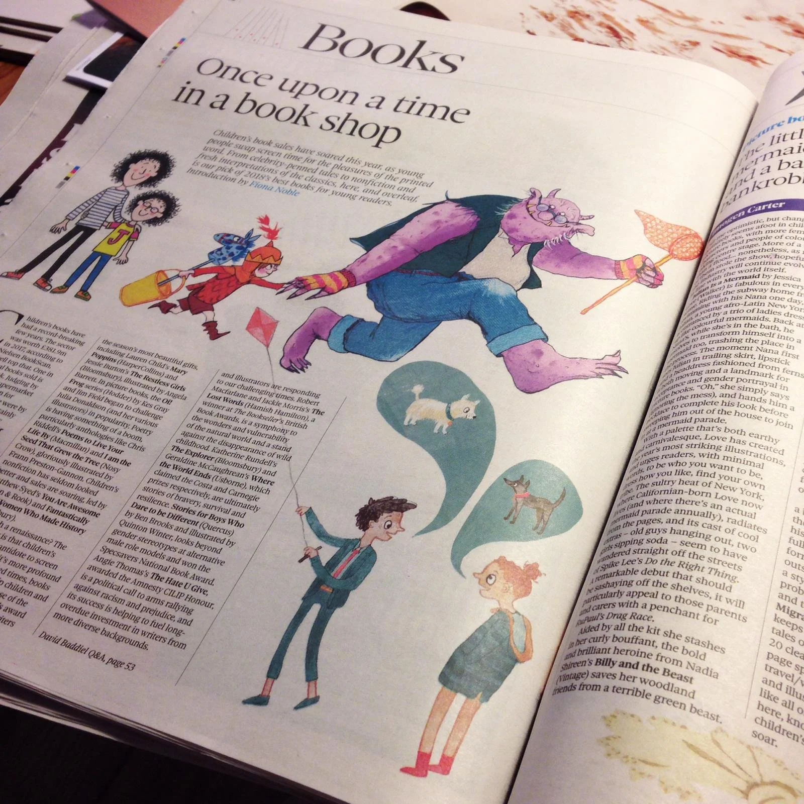 An open magazine or newspaper featuring an article titled "Books once upon a time in a book shop" with colorful illustrations of children and a friendly monster.