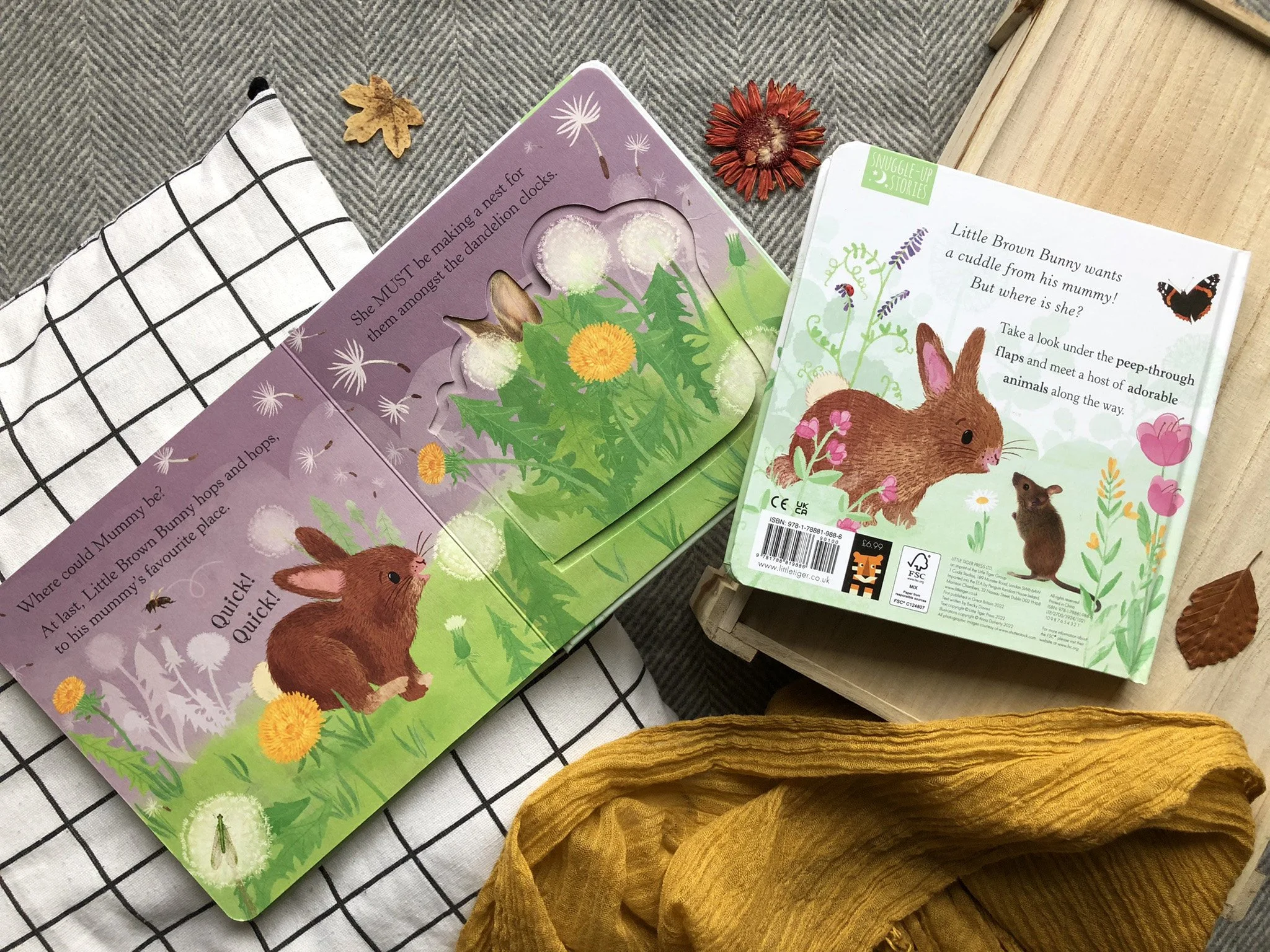 Open children's book with illustrations of a bunny and flowers on a table alongside a sock and a flower, partially visible.