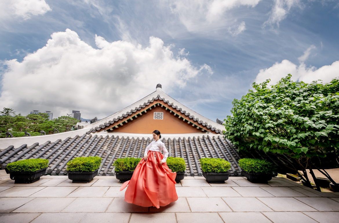 Korean hanbok fashion in a traditional hanok setting, featuring tiled roofs, garden elements, and cultural architecture. This image reflects Korean heritage, traditional clothing, and refined aesthetic rooted in history.