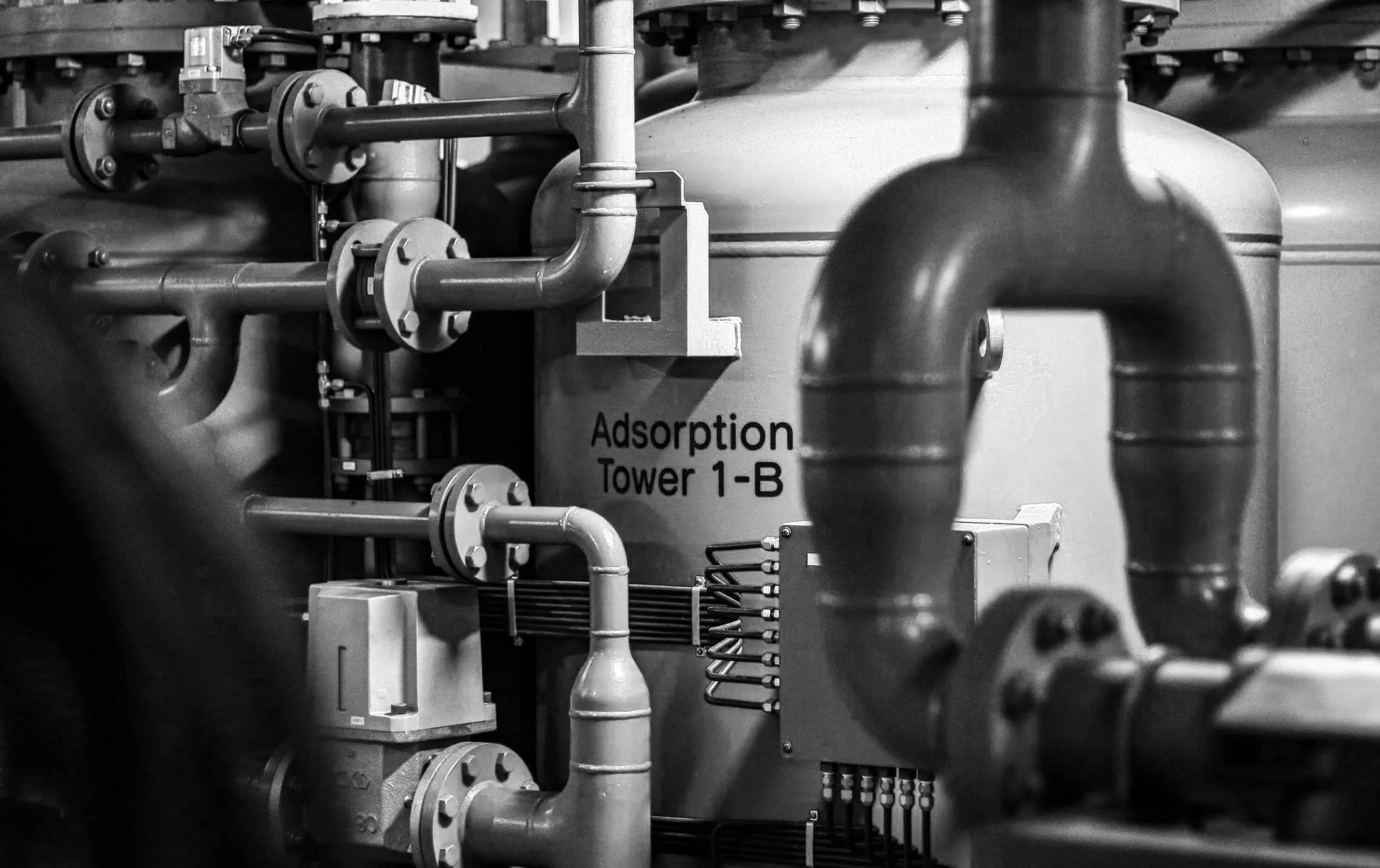 Black and white photo of industrial pipes and machinery labeled 'Adsorption Tower 1-B'.