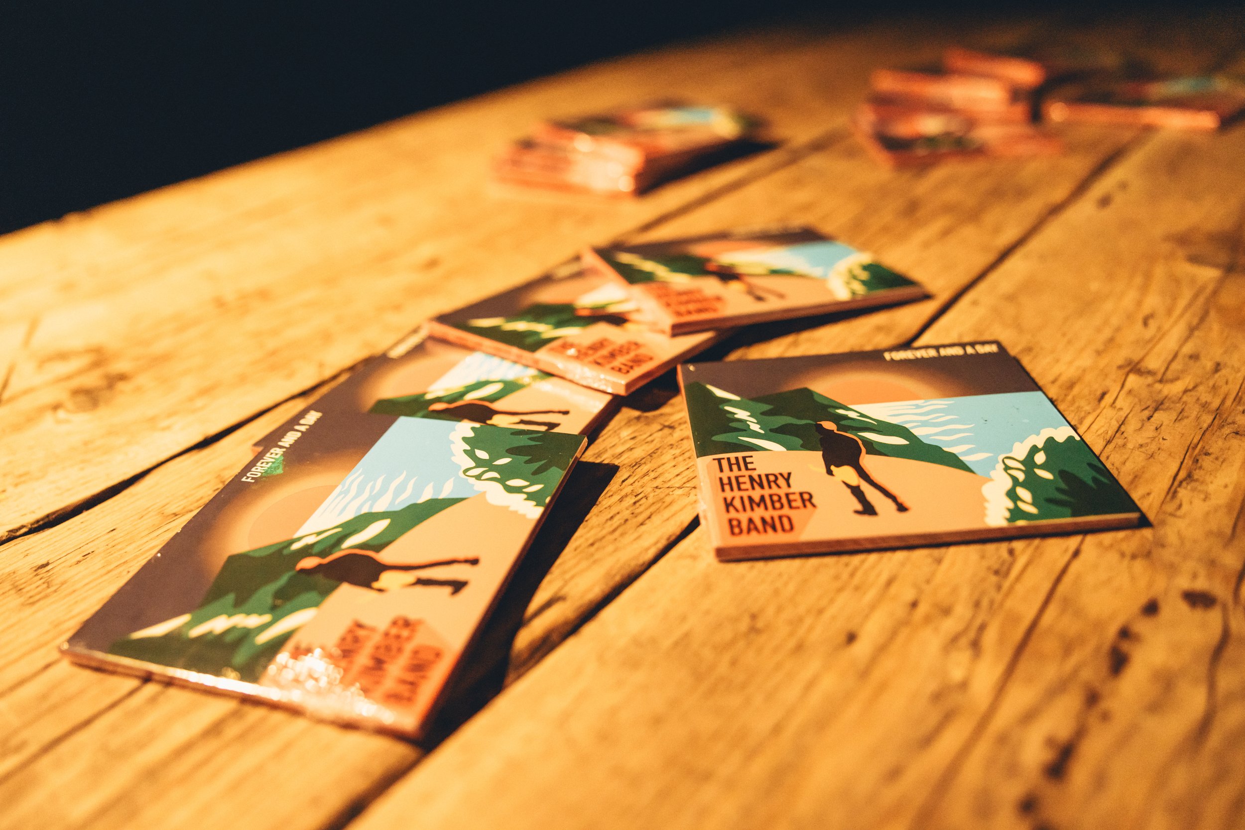 Colorful album covers with nature scene and a person walking along the coastline, scattered on a wooden table.