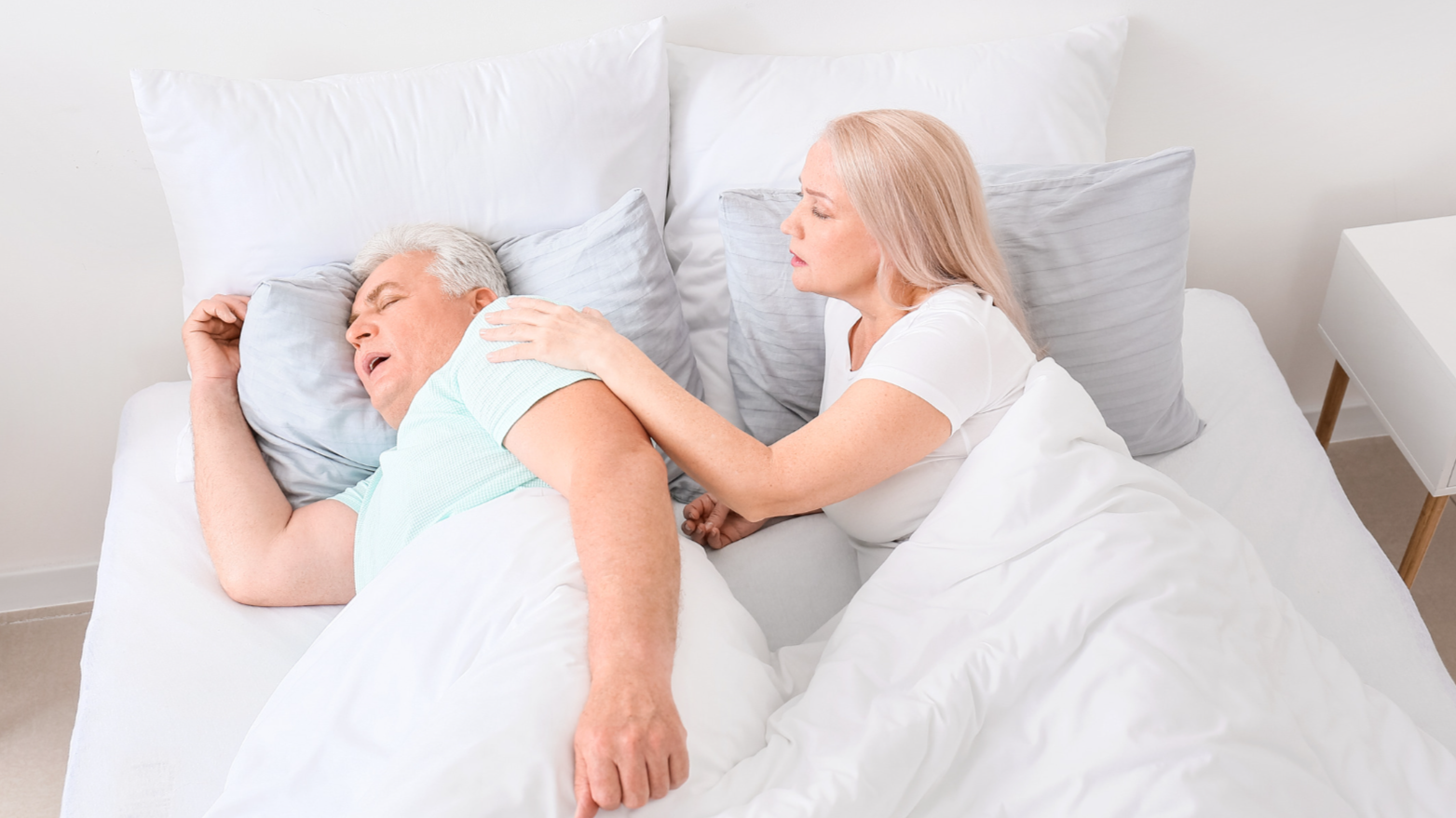couple in bed, man is snoring, wife is upset at his snoring and she is trying to wake him
