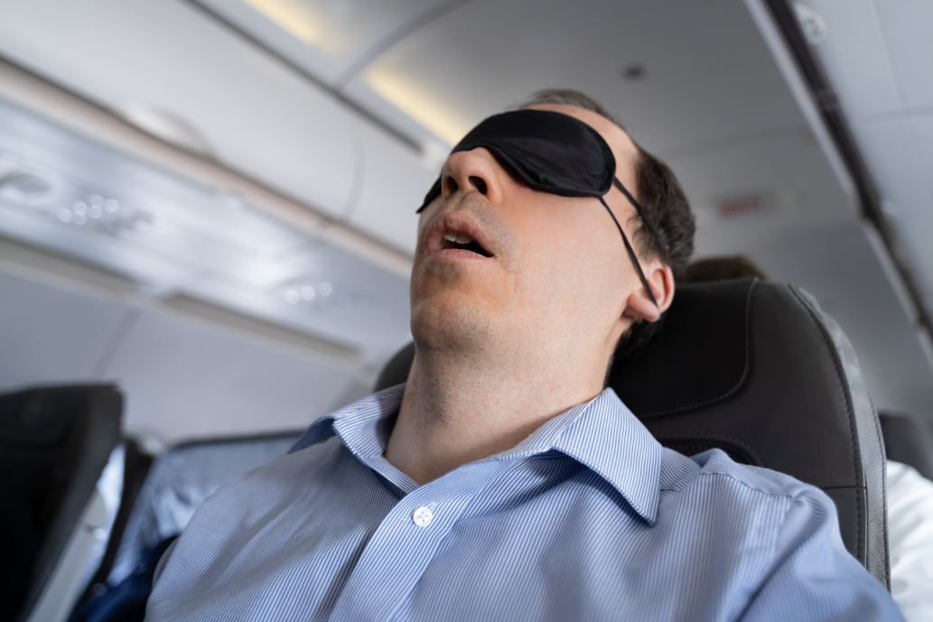 image of man snoring on a plane trying to combat jet lag, this article explains why snoring and sleep apnoea is worse when you have jetlag