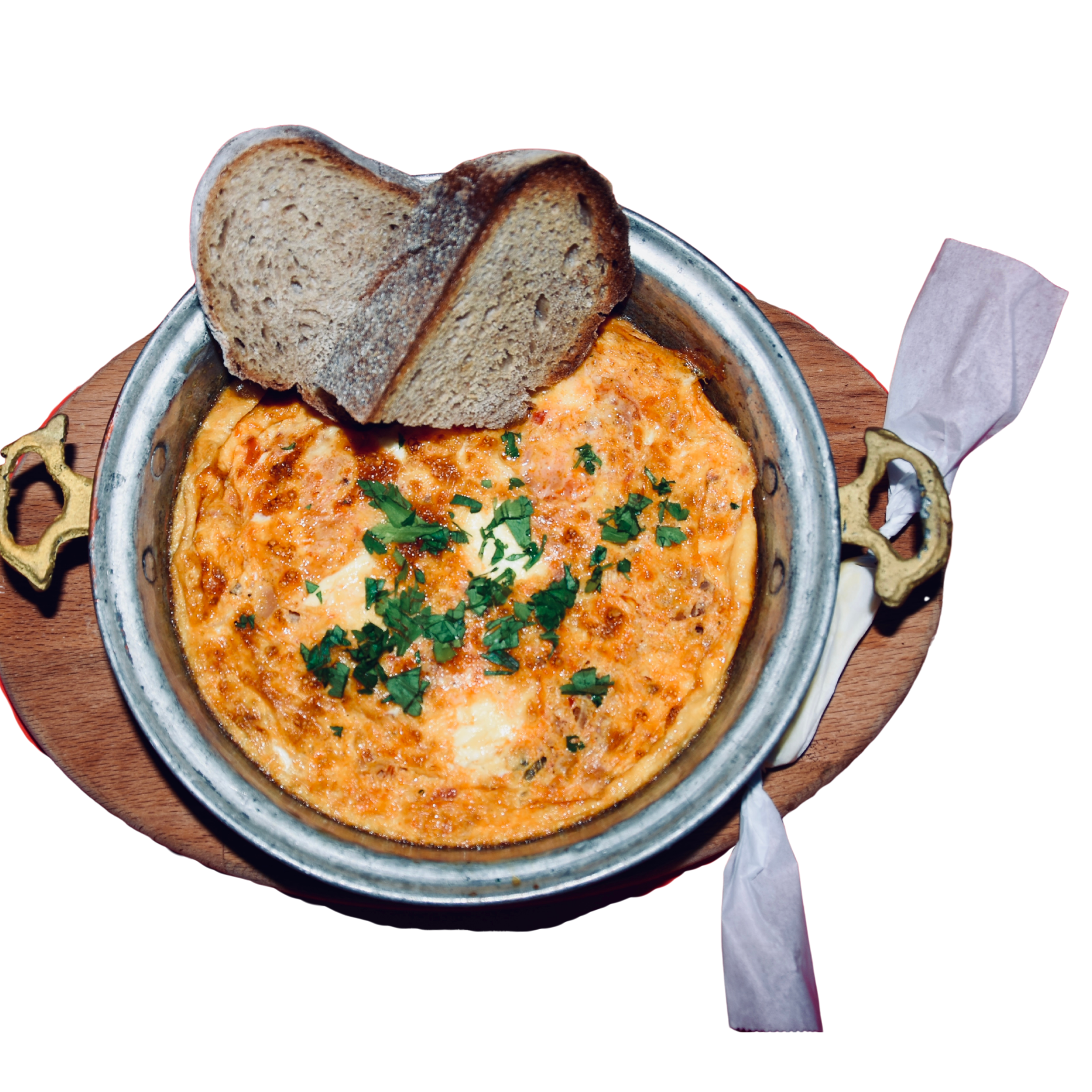 A bowl of cheesy baked dip garnished with chopped parsley, served with slices of whole wheat bread and surrounded by decorative dried pasta and napkins.