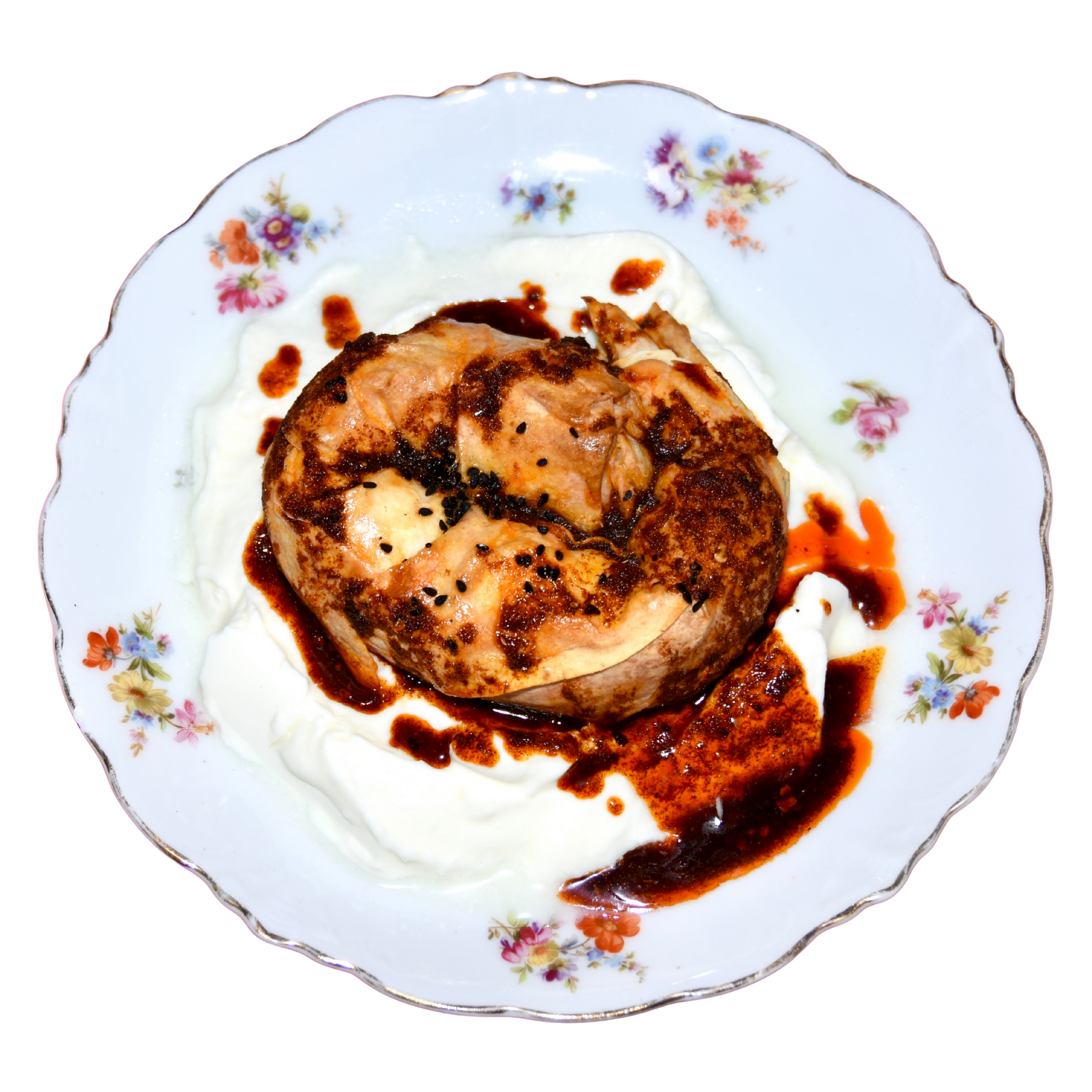 A floral patterned porcelain plate holding a piece of meat with sauce, around a serving of mashed potatoes drizzled with gravy.