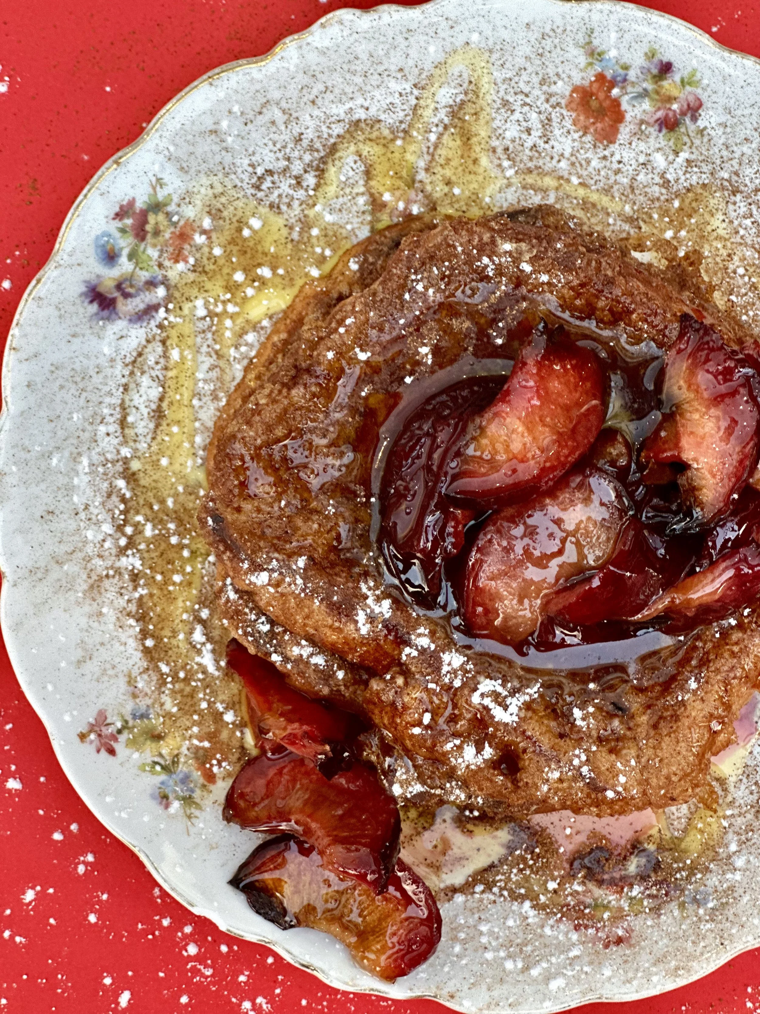 A plate with French toast topped with strawberries, syrup, and powdered sugar, set on a red surface.