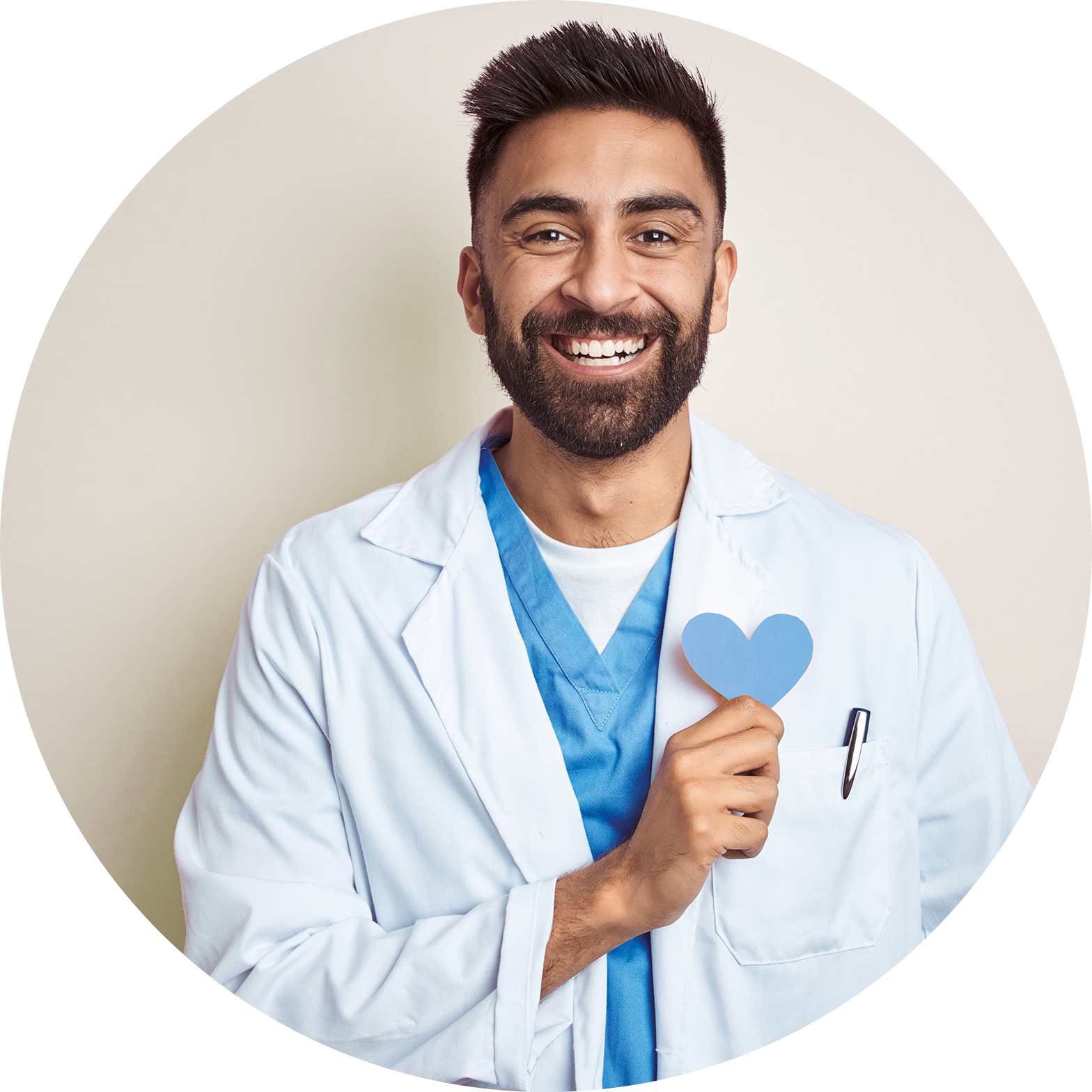 A smiling male doctor with a beard and short dark hair, wearing white medical coat and blue scrubs, holding a blue paper heart symbol in his right hand.