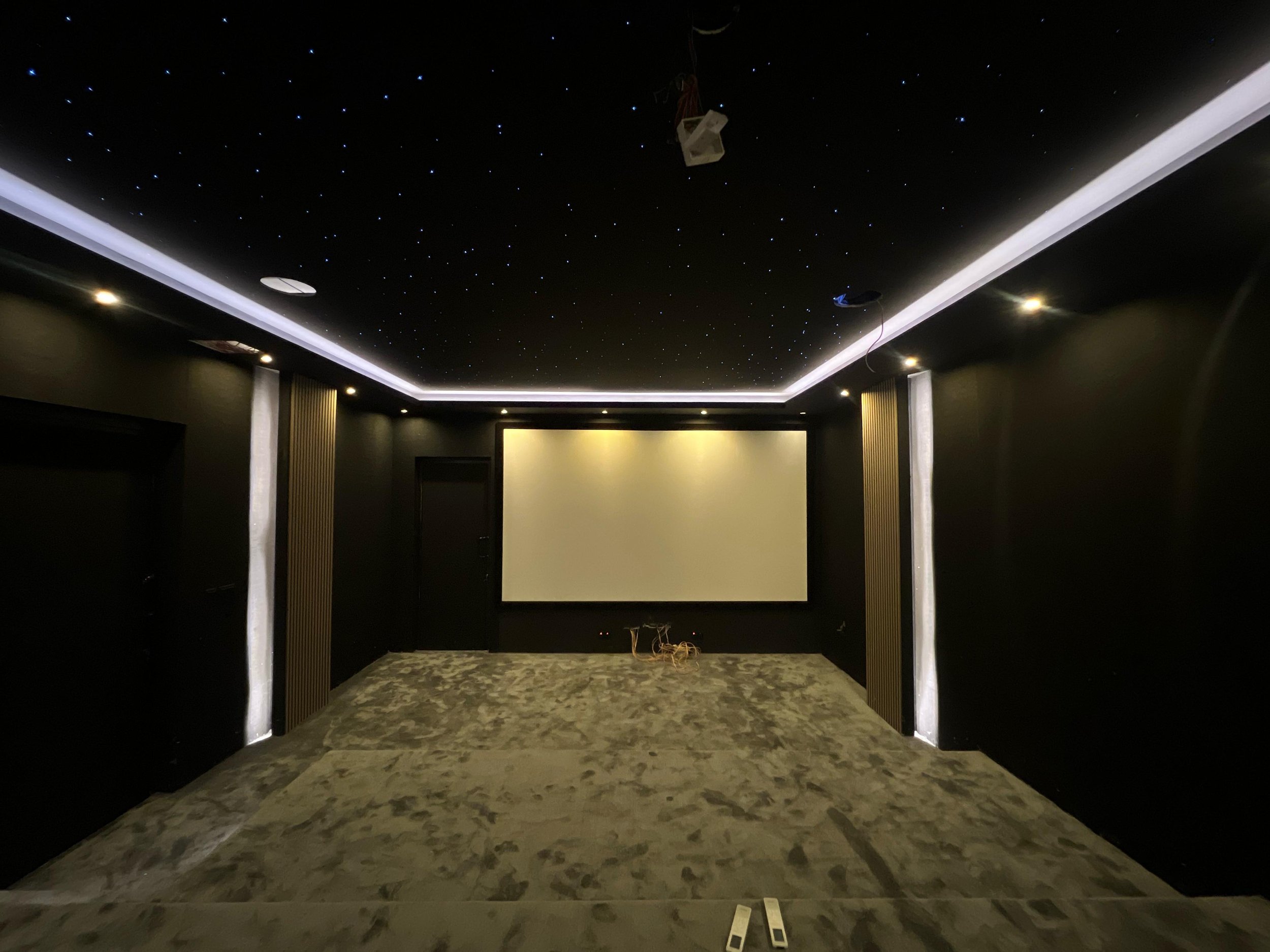 The ceiling is decorated with small star-like LED lights and has a moon-shaped light fixture. The walls are dark-colored with light-colored vertical panels. The room appears to be under construction or renovation, with exposed wiring and construction materials on the floor.