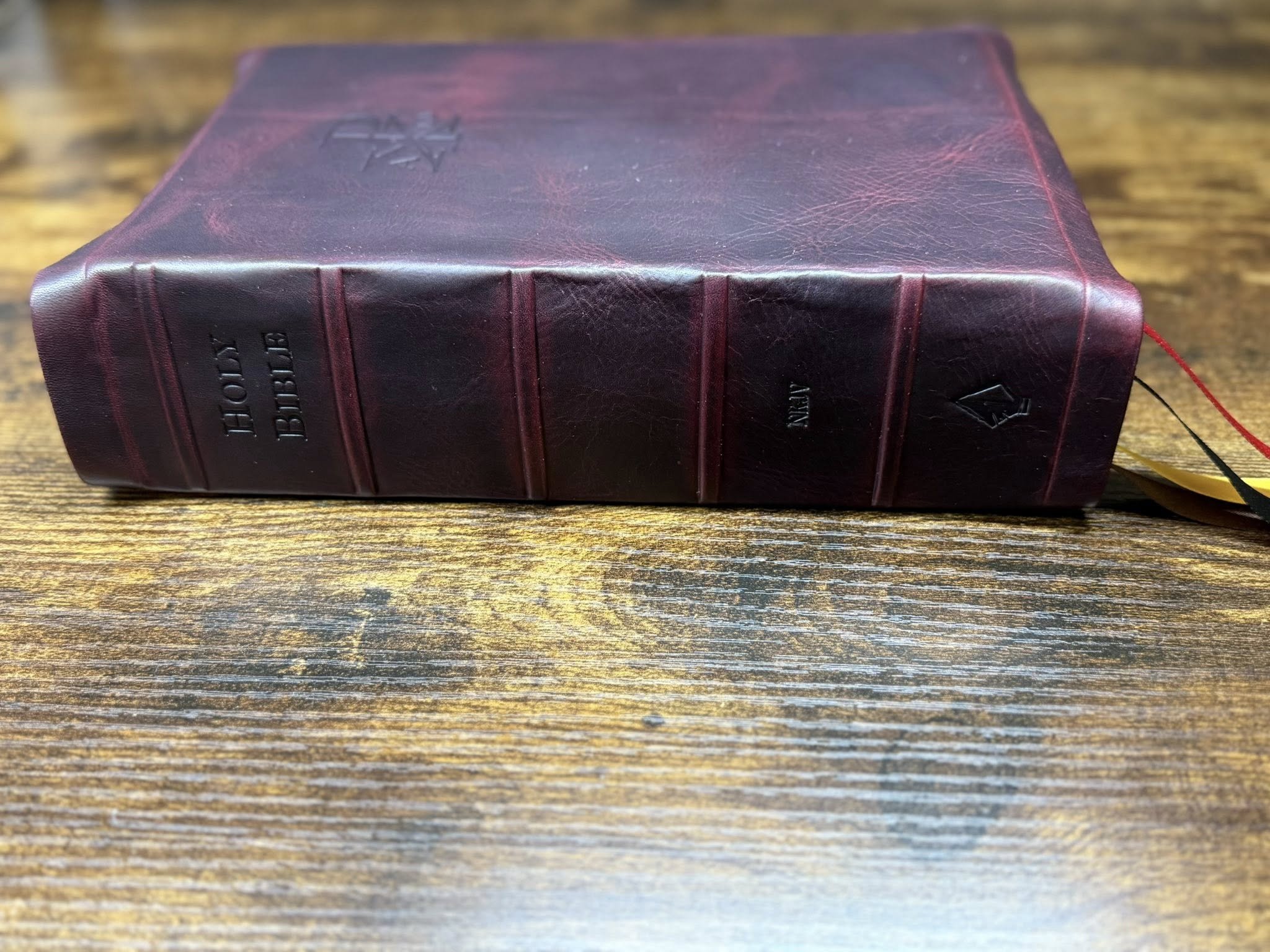 A closed, dark purple hardcover book with the title "The Bible" embossed on the spine, resting on a wooden surface.
