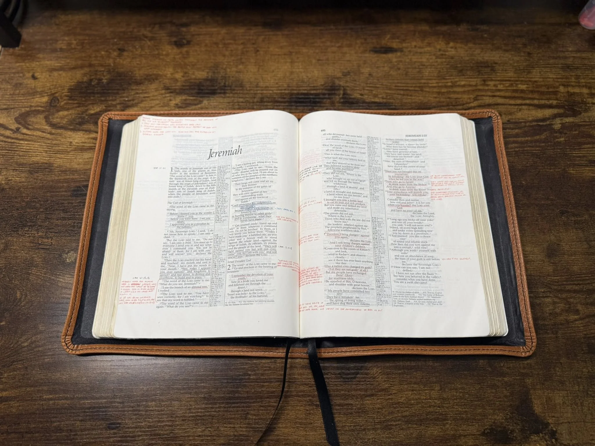 Open Bible opened to the book of Jeremiah, with red-inked handwritten notes in the margins, placed on a dark wooden table.