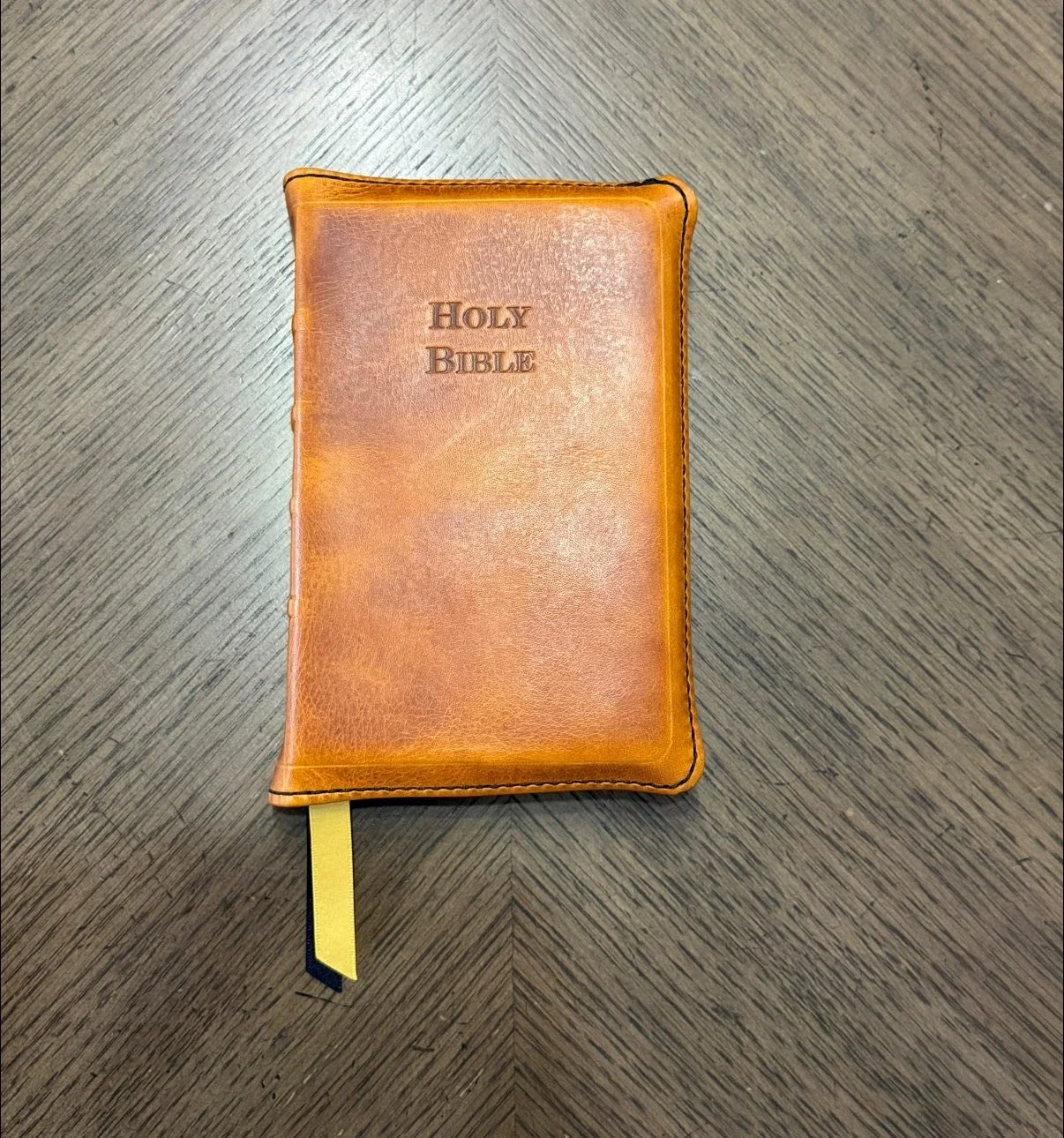 A brown leather-bound Holy Bible with a yellow ribbon bookmark, placed on a dark wooden surface.