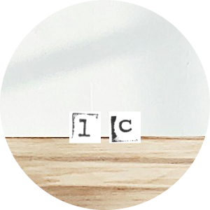 Close-up of a wooden surface with a small paper or sticker showing part of the letter 'I' and a partial 'C' on it.
