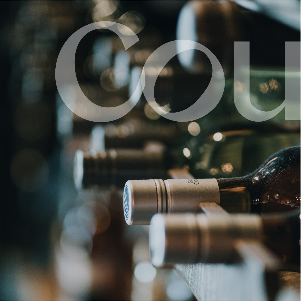 Close-up of a wine bottle on a wine rack, with other bottles blurred in the background.