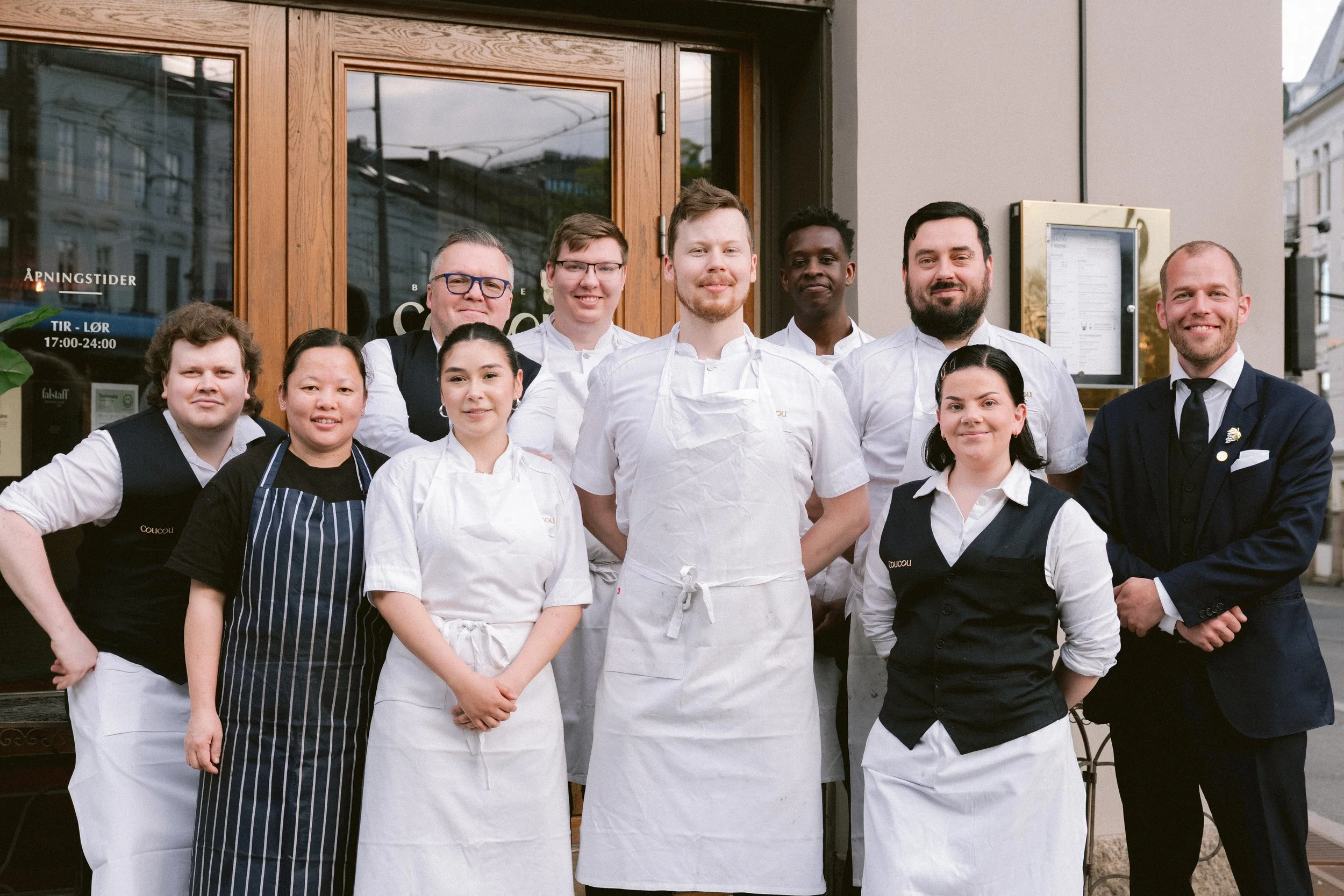 Group of nine people, including chefs and wait staff, standing outside a restaurant, smiling at the camera.