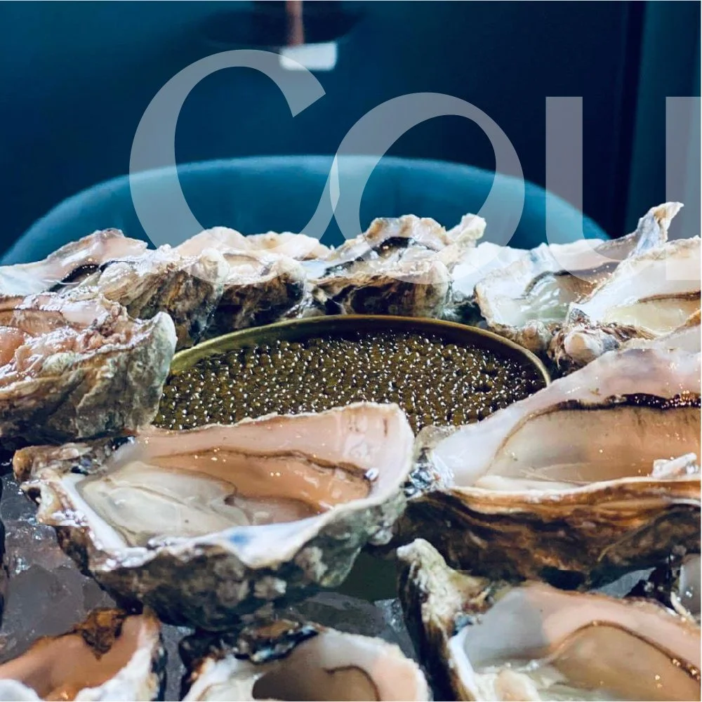 A bowl of oysters on a table, with several opened oyster shells surrounding it.
