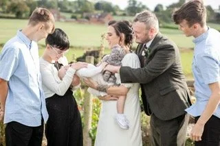 A bride and groom with four children outdoors, holding a white puppy.